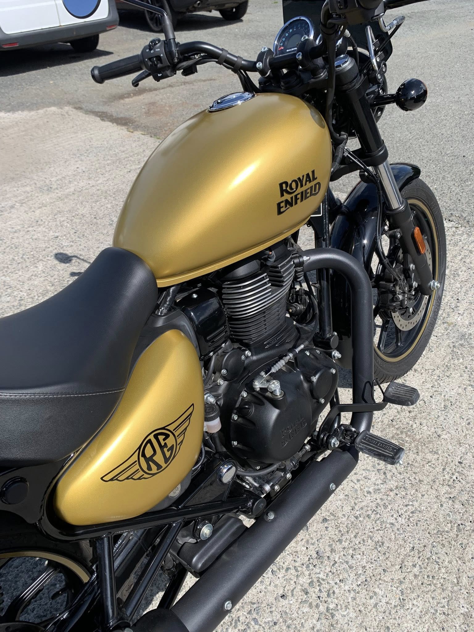 Gold Royal Enfield motorcycle parked on a concrete surface, showing the fuel tank, seat, and engine.