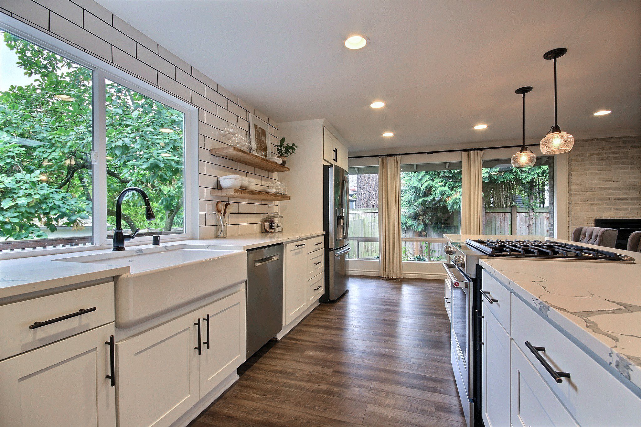 This large open concept Kingsgate, Kirkland family room/dining room/kitchen area came to life by taking down all the dividing walls, moving the pantry to be wide instead of deep, adding can lighting, pendants, a chandelier, and new flooring. The whit