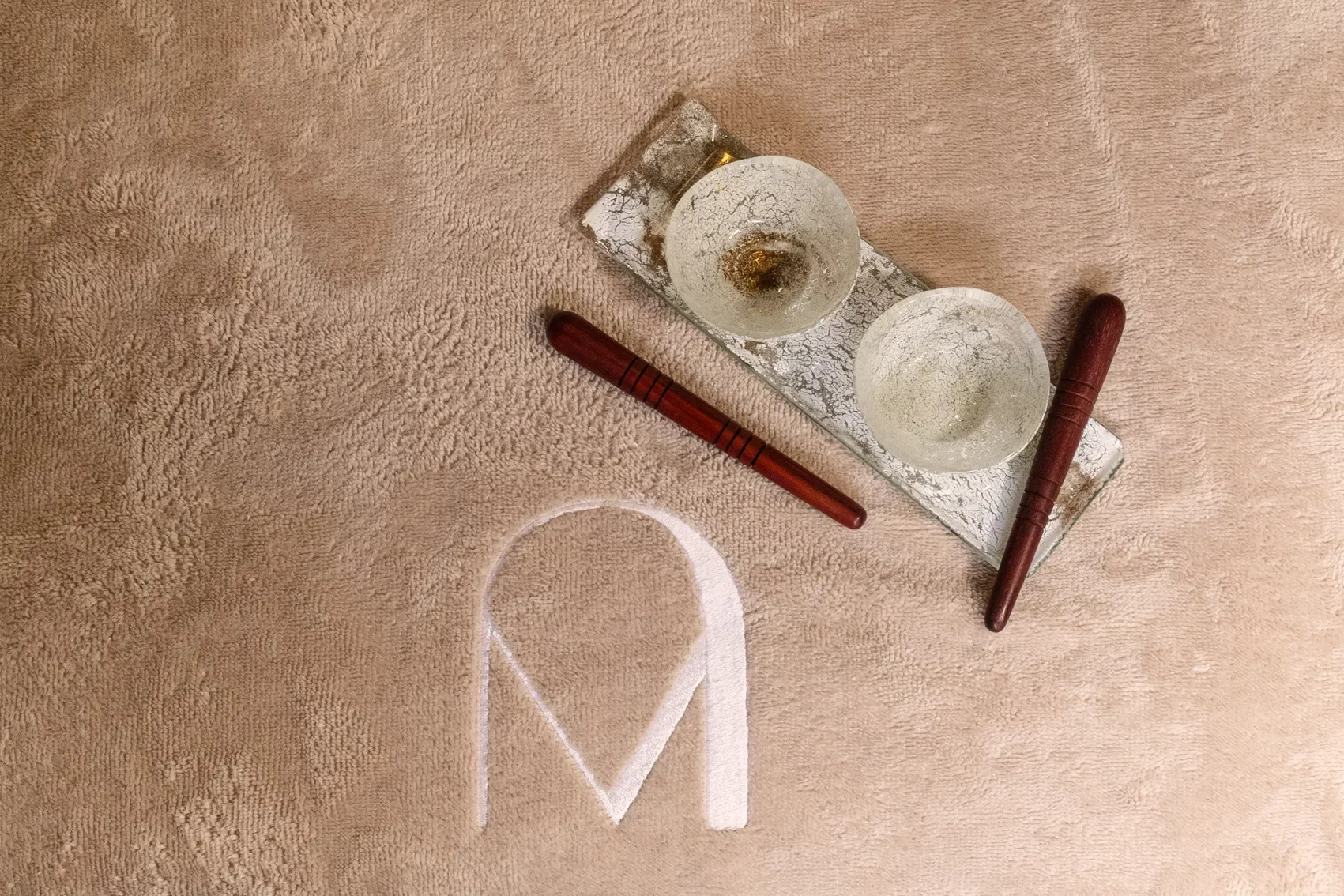 Deux bols en verre avec une décoration craquelée, sur un plateau en verre, deux bâtons en bois, et un tapis beige avec une ligne blanche.