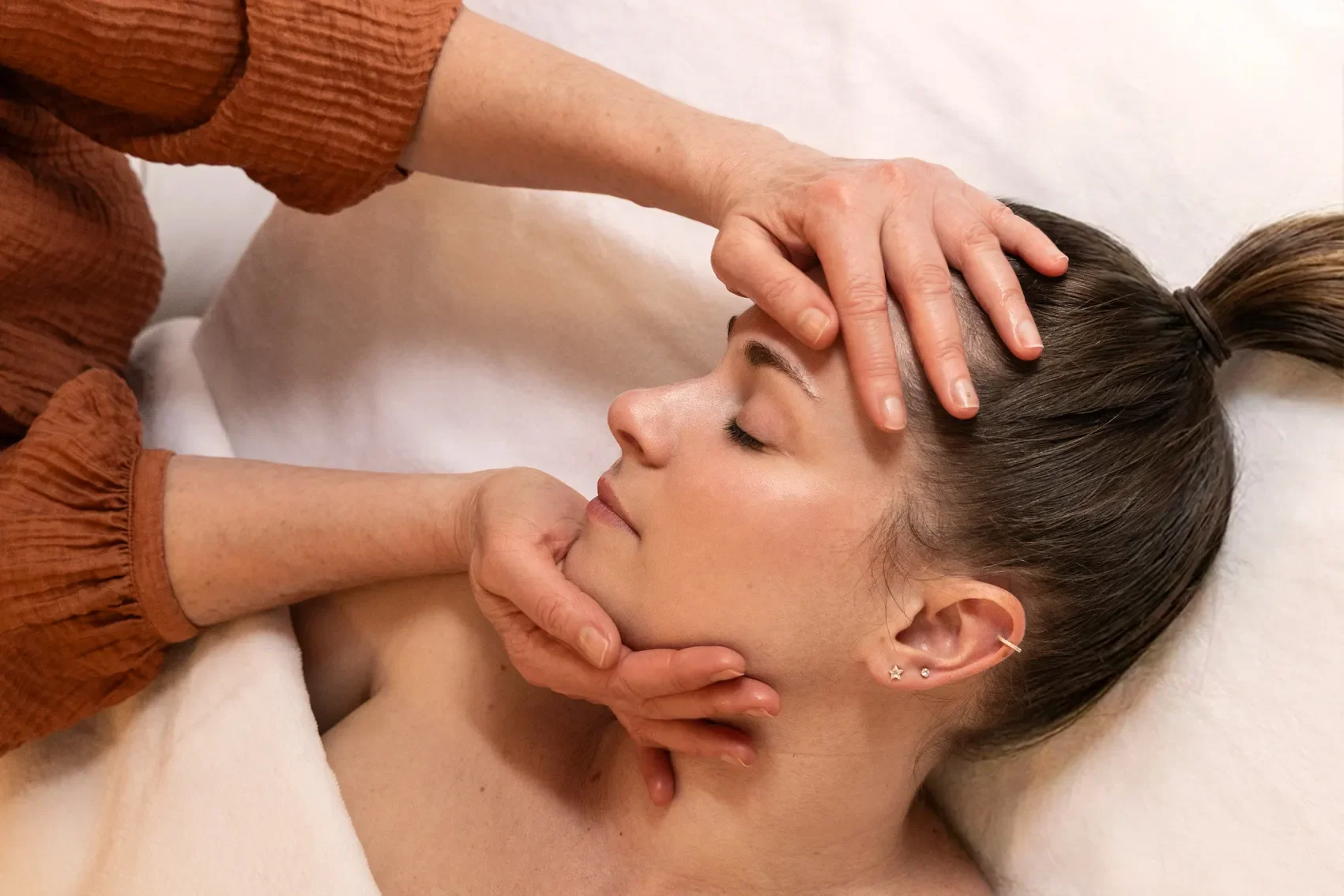 Une femme reçoit une séance de soins ou de massage, allongée sur le dos, avec une personne qui lui masse la tête et le visage.