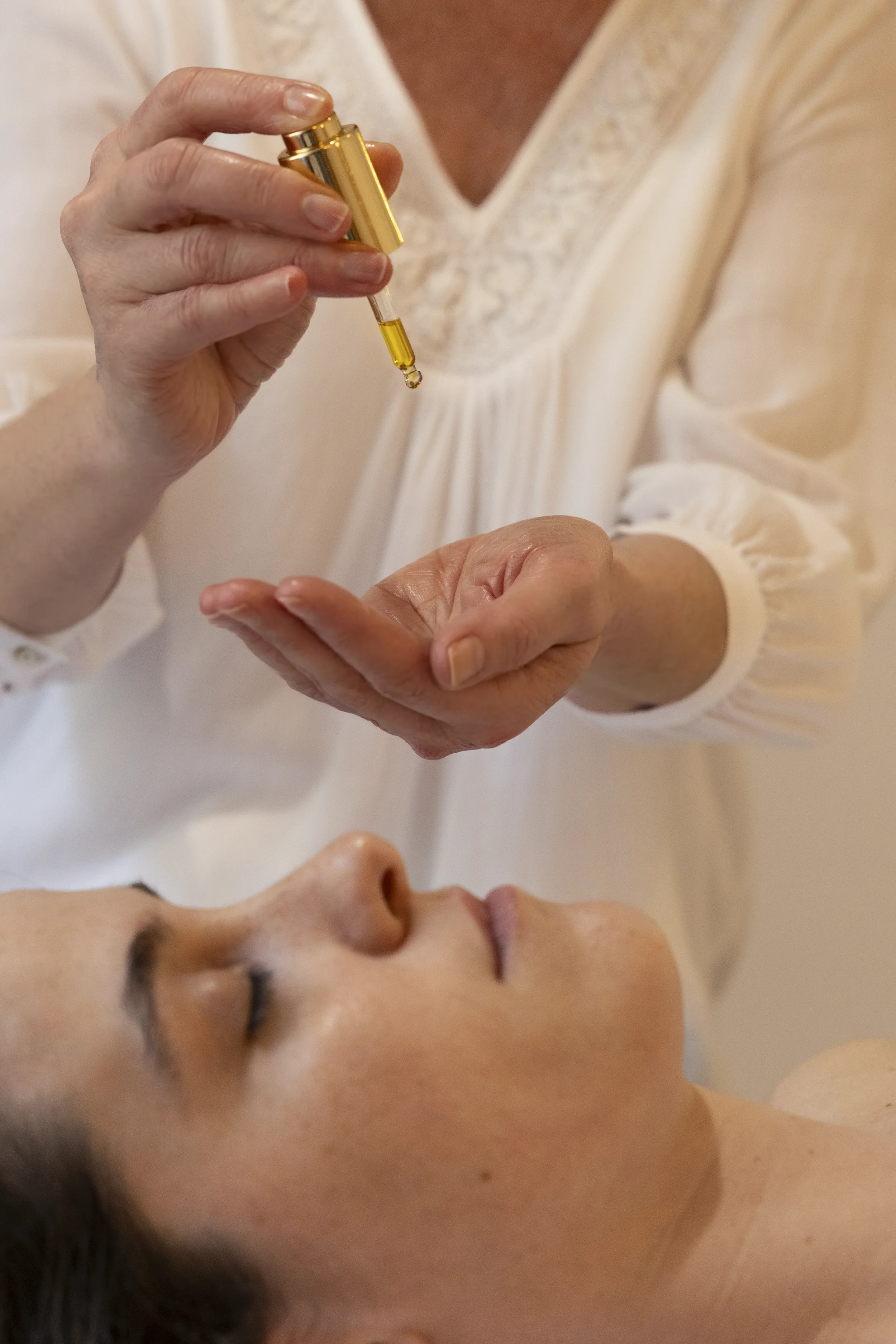 Une personne détend une autre personne allongée à qui on administre une injection ou un traitement avec une pipette contenant un liquide jaune.