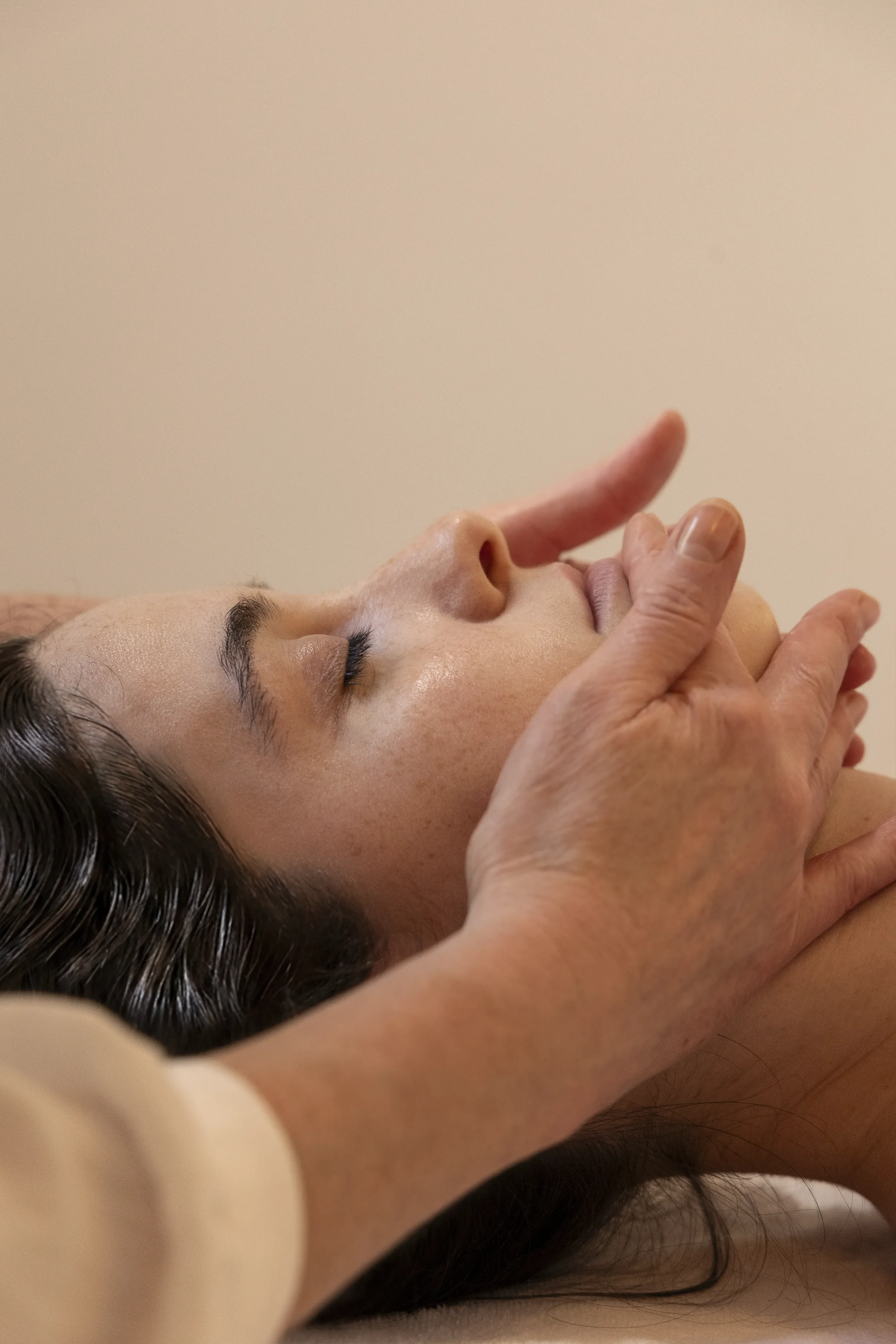Une personne repose les yeux fermés, tandis qu'une autre personne manipule doucement son visage avec la main, dans une ambiance calme et relaxante.