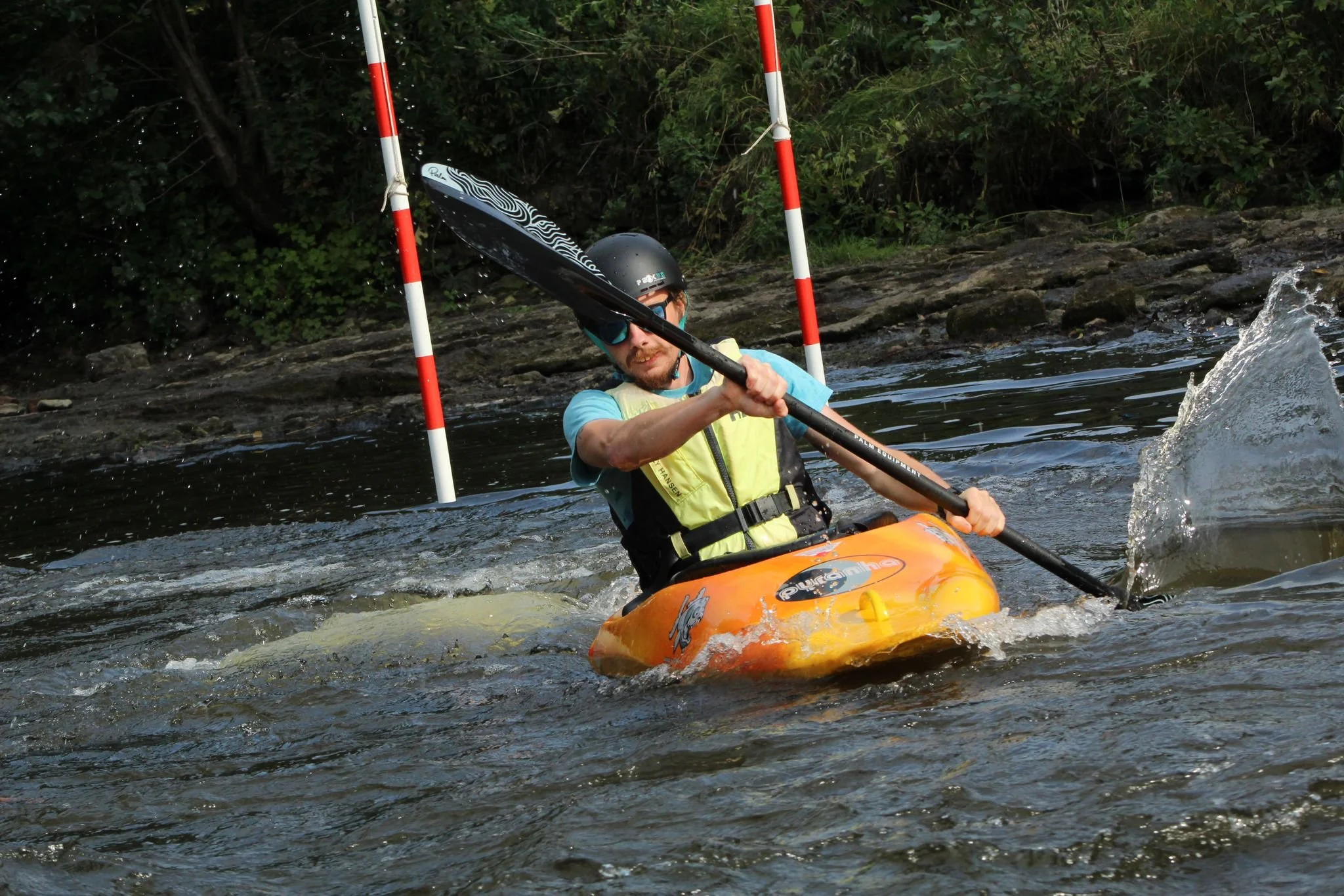 Person in a yellow kayak navigating through a waterway with a slalom gate in the background.