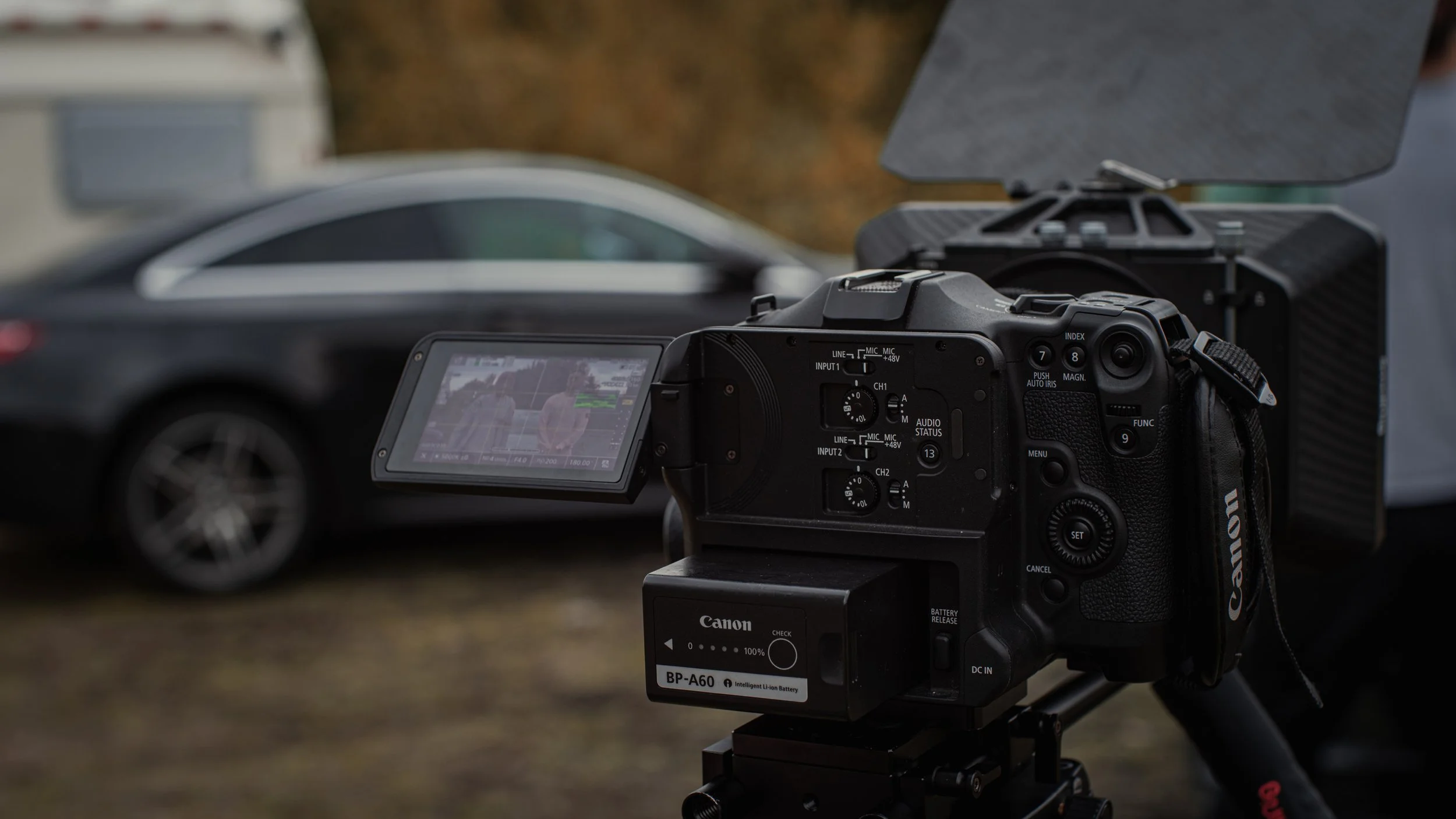 A camera setup on a tripod capturing a scene featuring a car and a person, with the scene viewed on the camera's display screen.