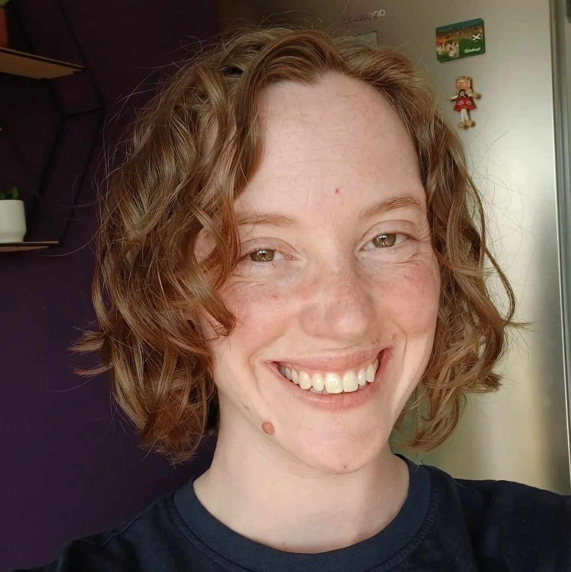 A smiling woman with curly red hair and freckles, wearing a black shirt,