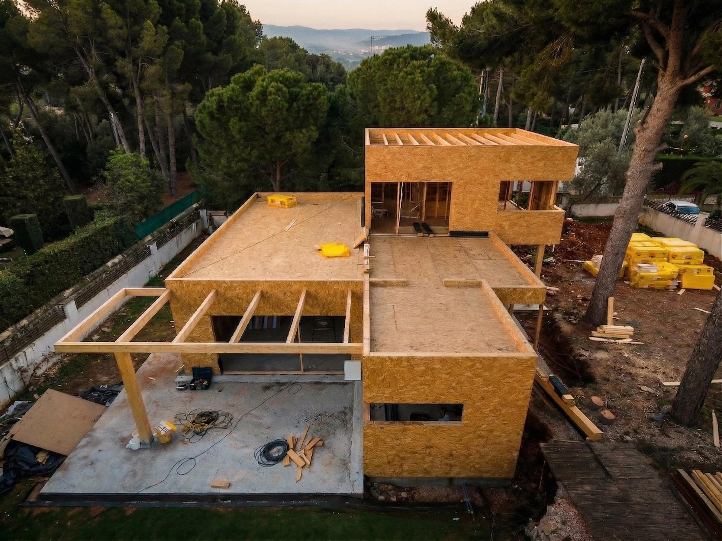 Vista aérea de una casa en construcción con estructura de madera en un entorno boscoso.