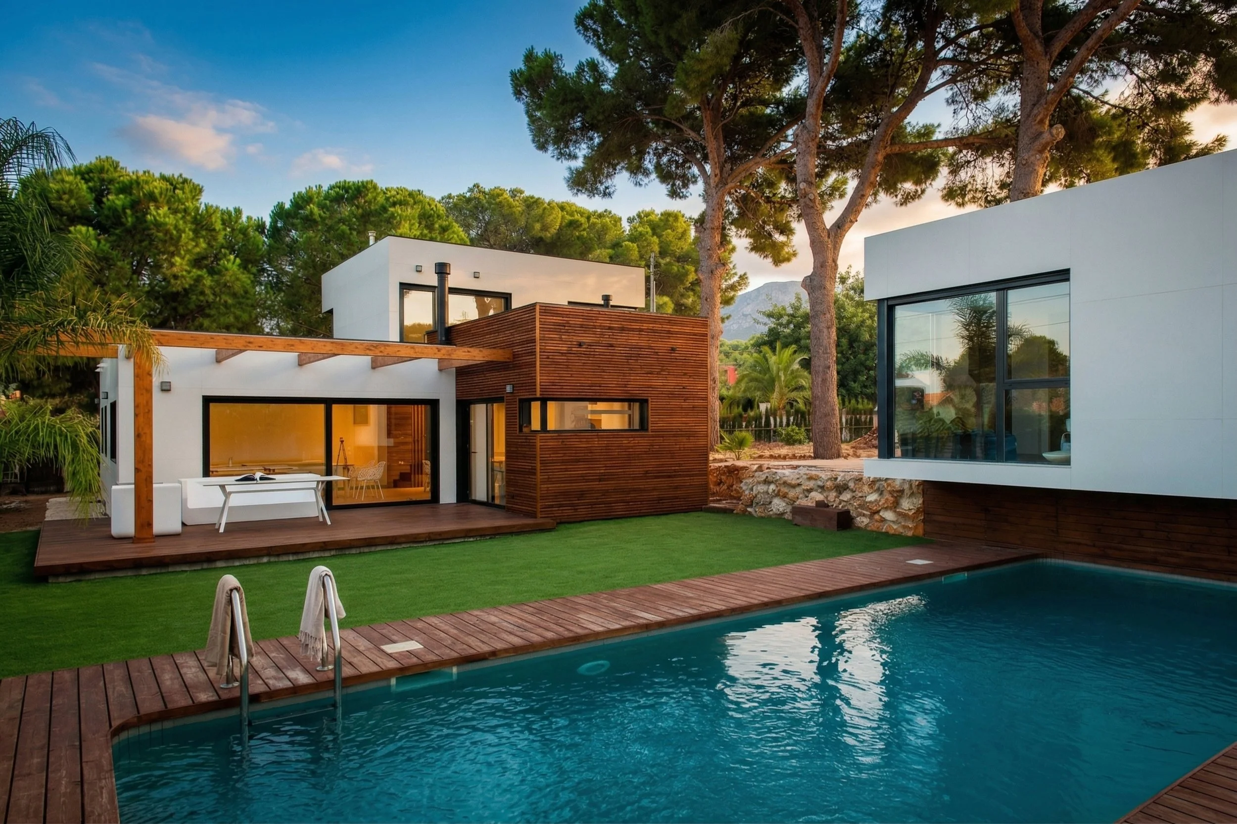 Casa moderna con piscina en el jardín, rodeada de árboles y naturaleza, con cielo despejado al atardecer.