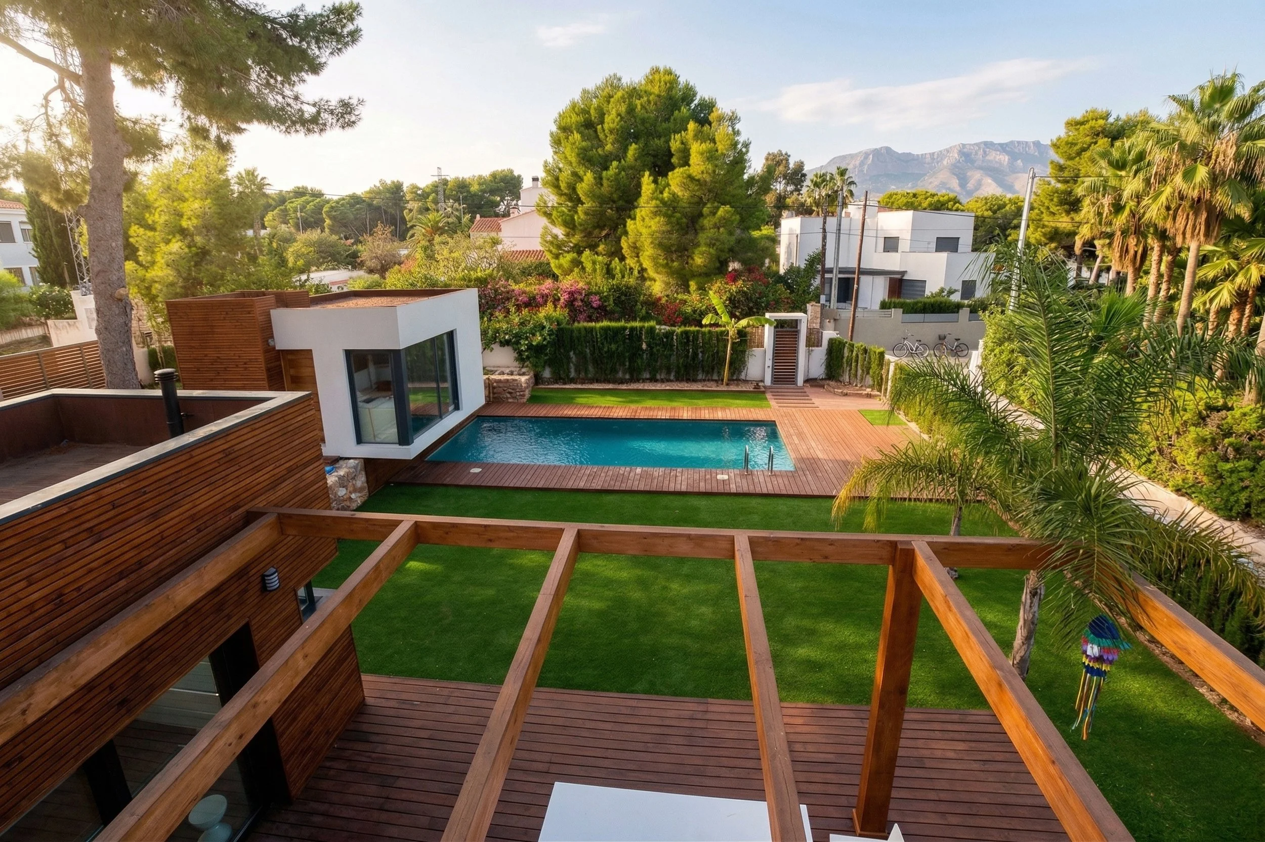 Vista desde arriba de un patio con piscina, césped, árboles y casas modernas en un ambiente cálido y soleado en un vecindario residencial.