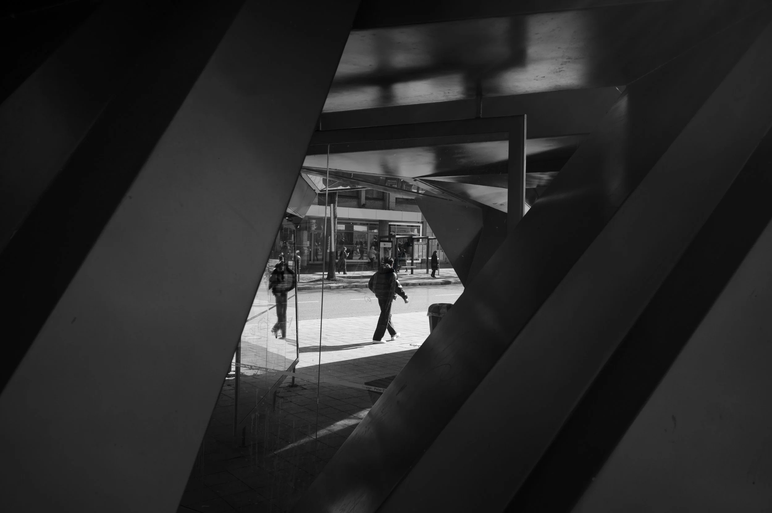 Through the structures of the busstation Elissenbrunnen Aachen a person walks by  and his reeflection in glas