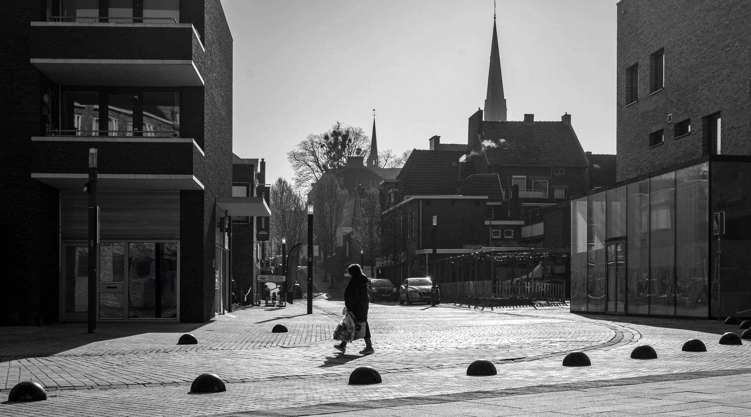 A lady with shopping bags crossing a square Backlited Through some modern buildings just outside of the Aachen City Centre.