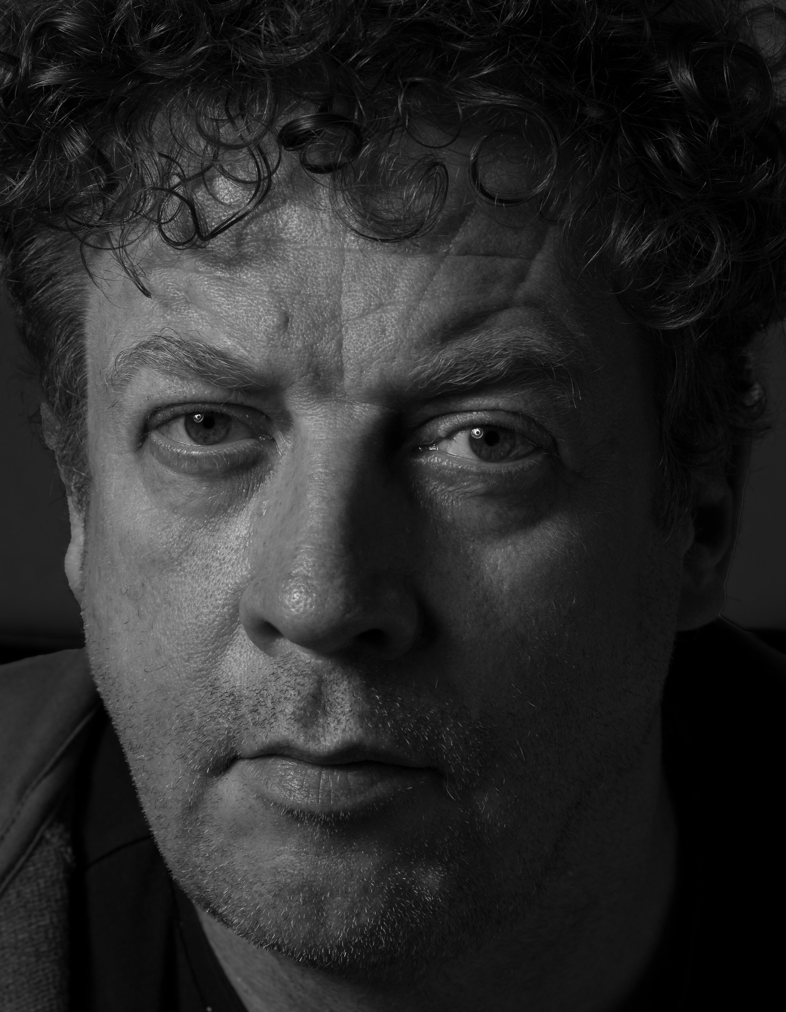 Close-up black and white photo of a man's face, focusing on the upper half, showing his eyes, eyebrows, and hair with curly texture.