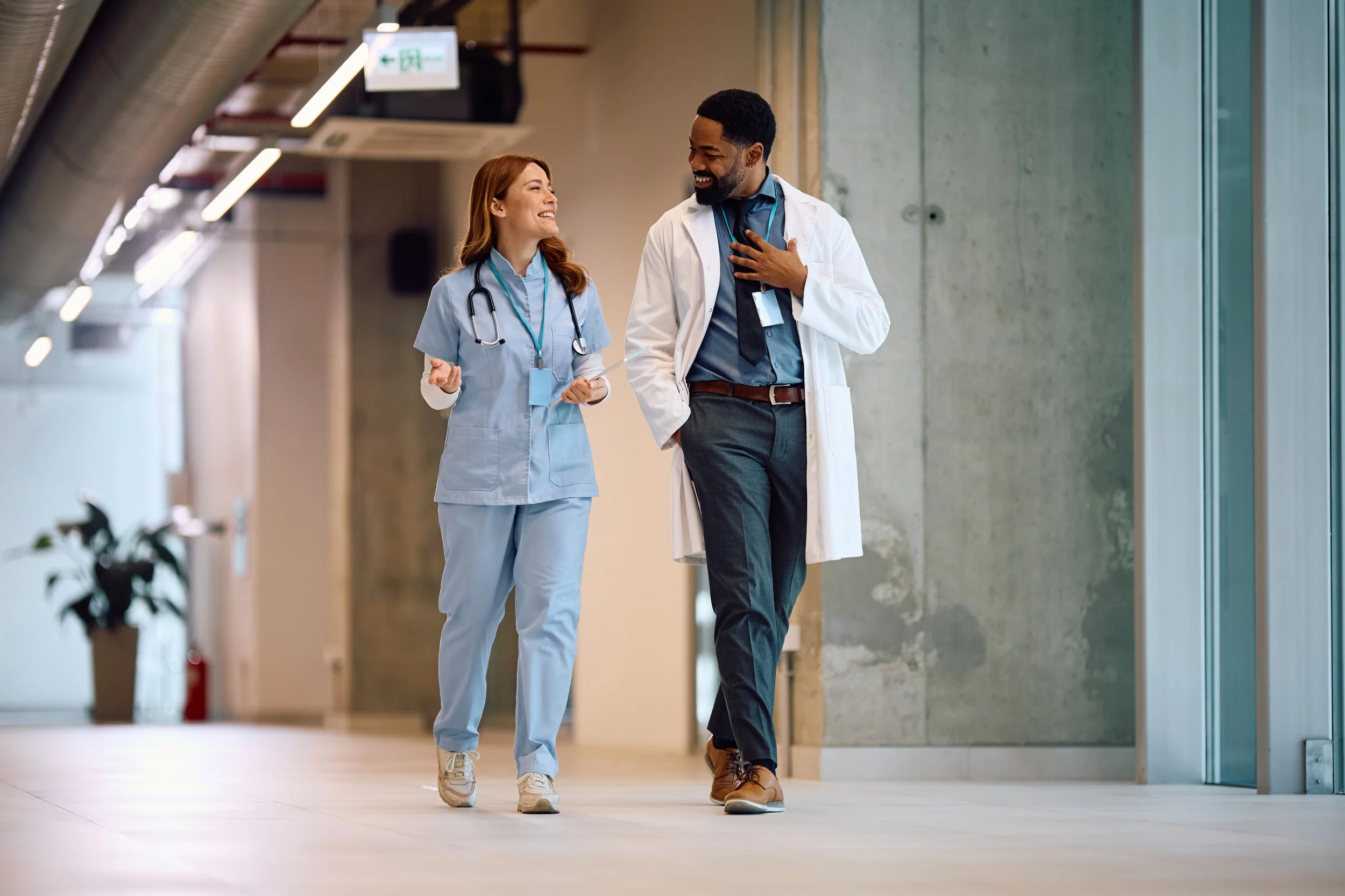 A doctor and nurse smiling together in a healthcare setting, representing collaboration and support provided by a rural healthcare advisory firm.