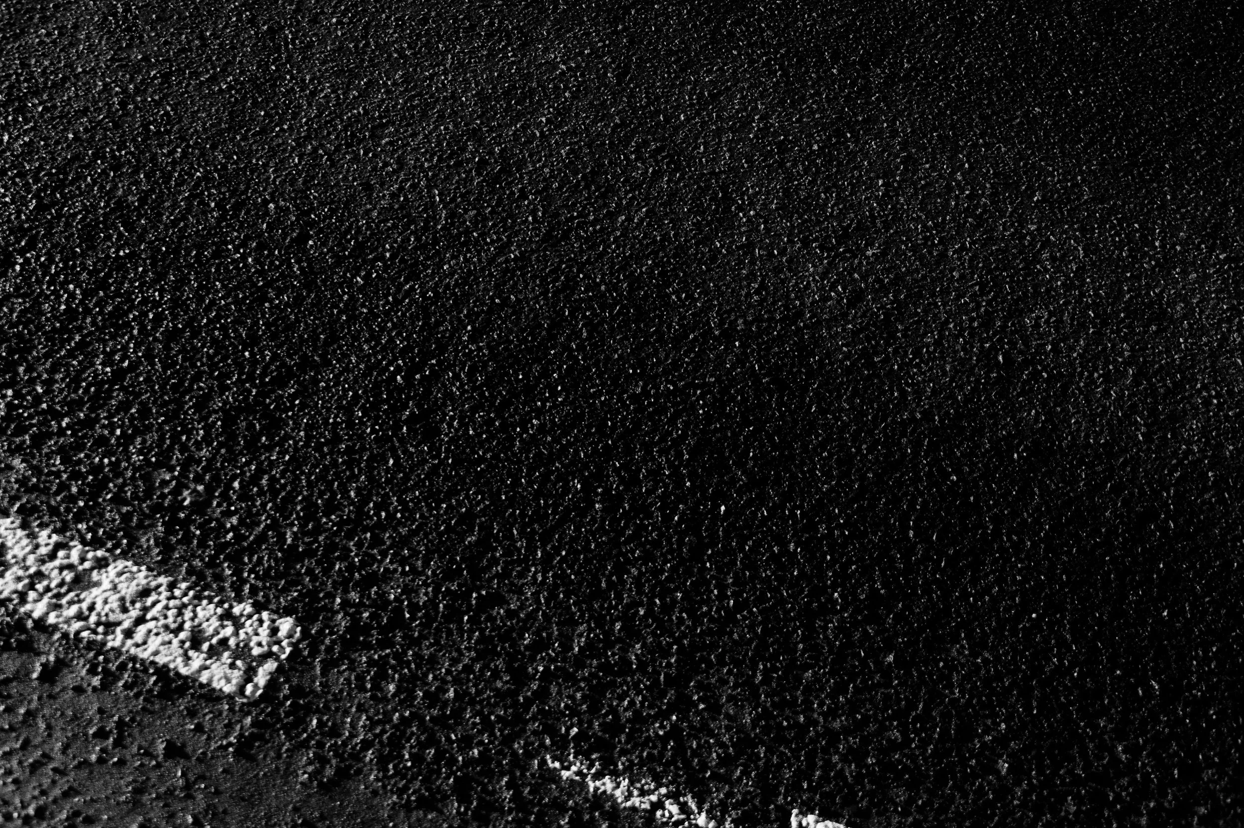 A close-up of a black asphalt road surface with granules and texture visible.