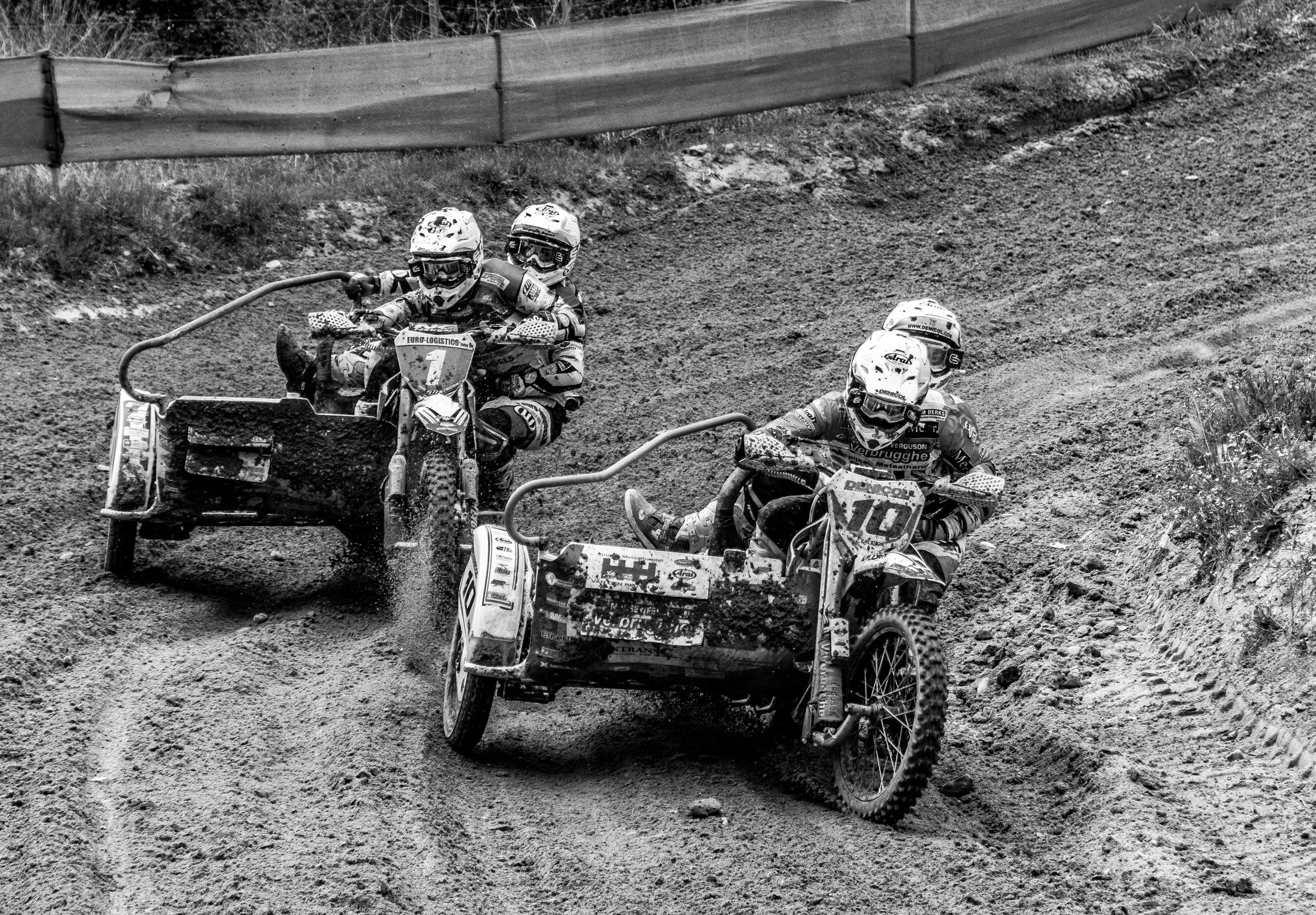 Dos motociclistas en un terreno de tierra con sidecars, participando en una carrera de velocidad en circuito de tierra.