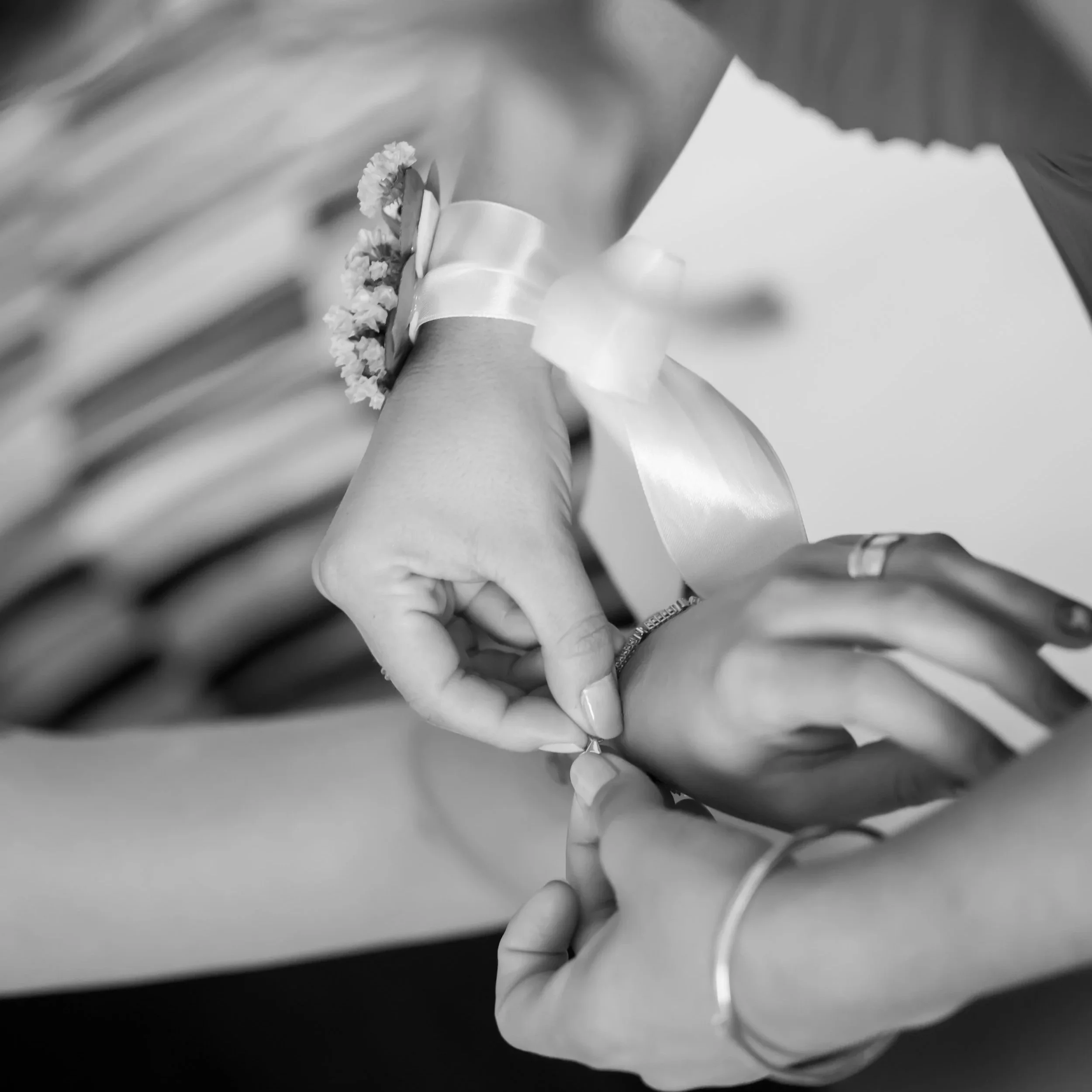 Persona colocando una alianza en el dedo de otra persona, en un entorno que parece ser una celebración, adornada con una pulsera de flores y un lazo de satén.