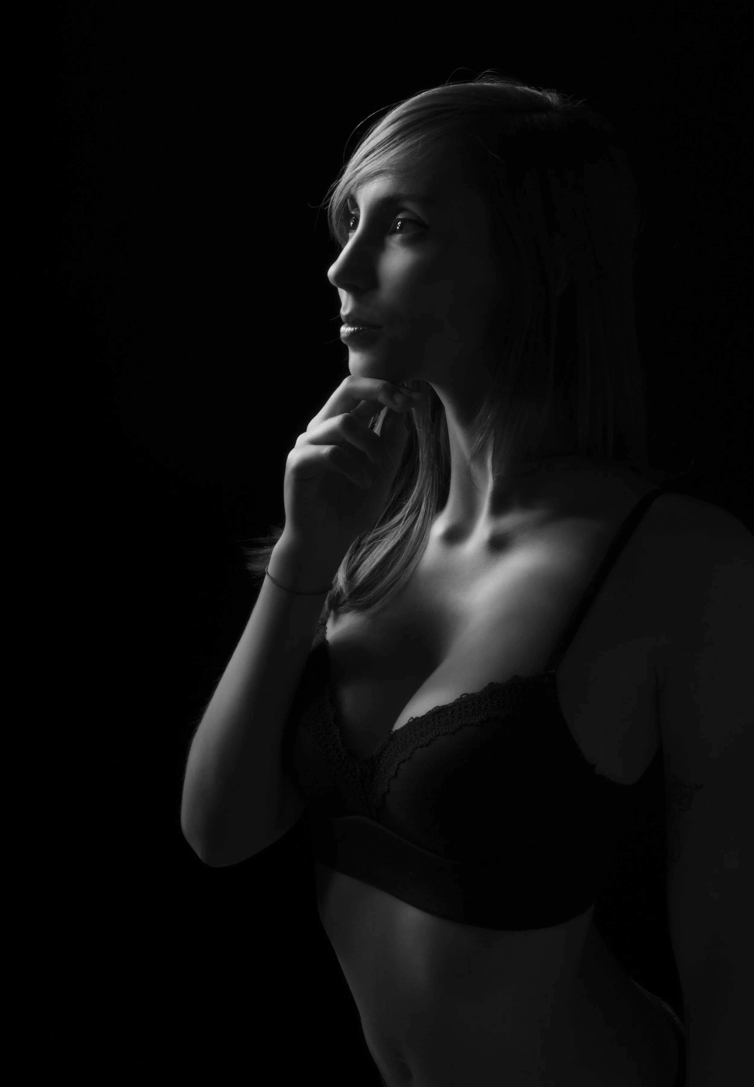 Retrato en blanco y negro de una mujer con cabello largo, en actitud pensativa, usando ropa de lencería, con fondo negro.