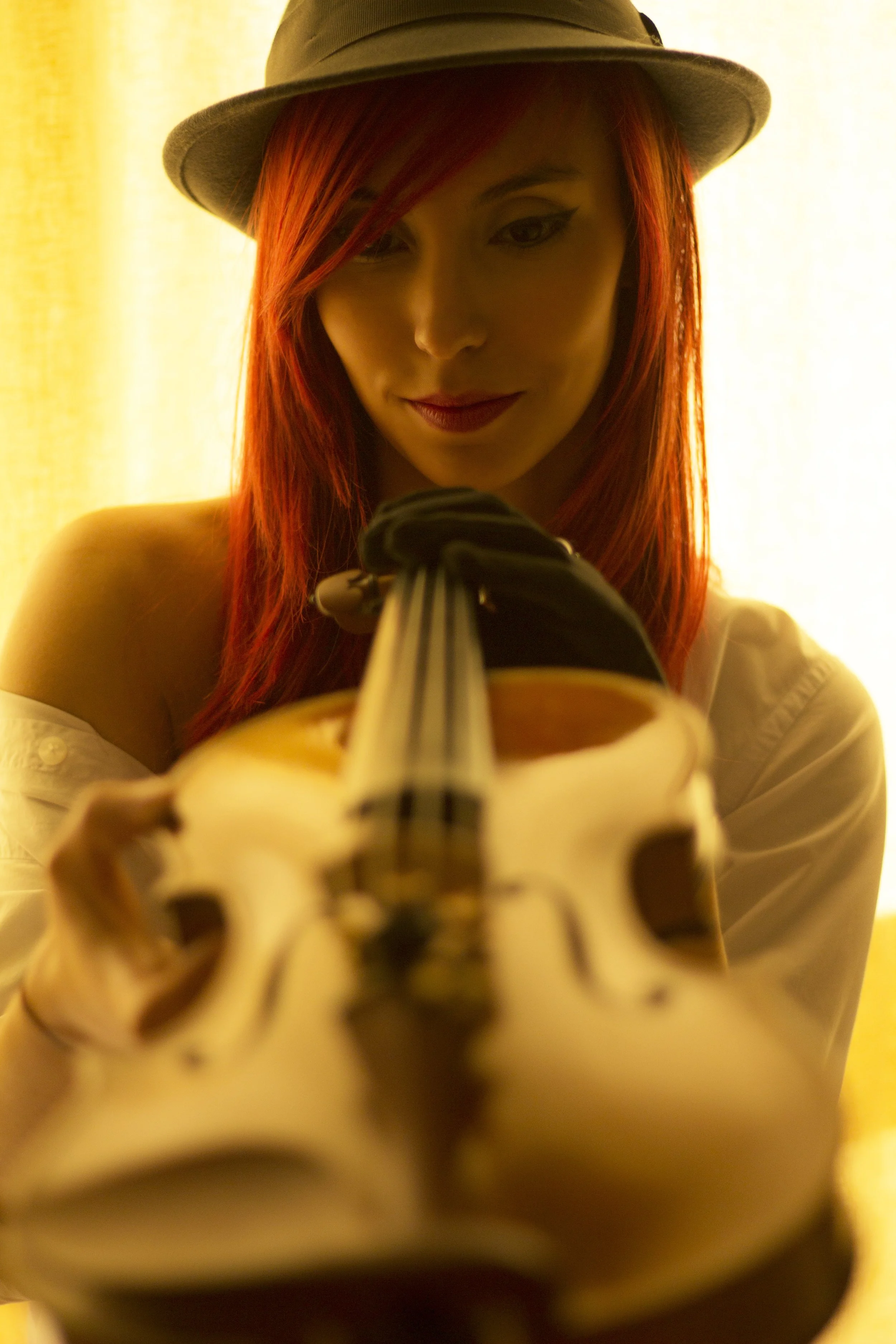 Mujer con cabello rojo, sombrero y guantes, posando con un violín.