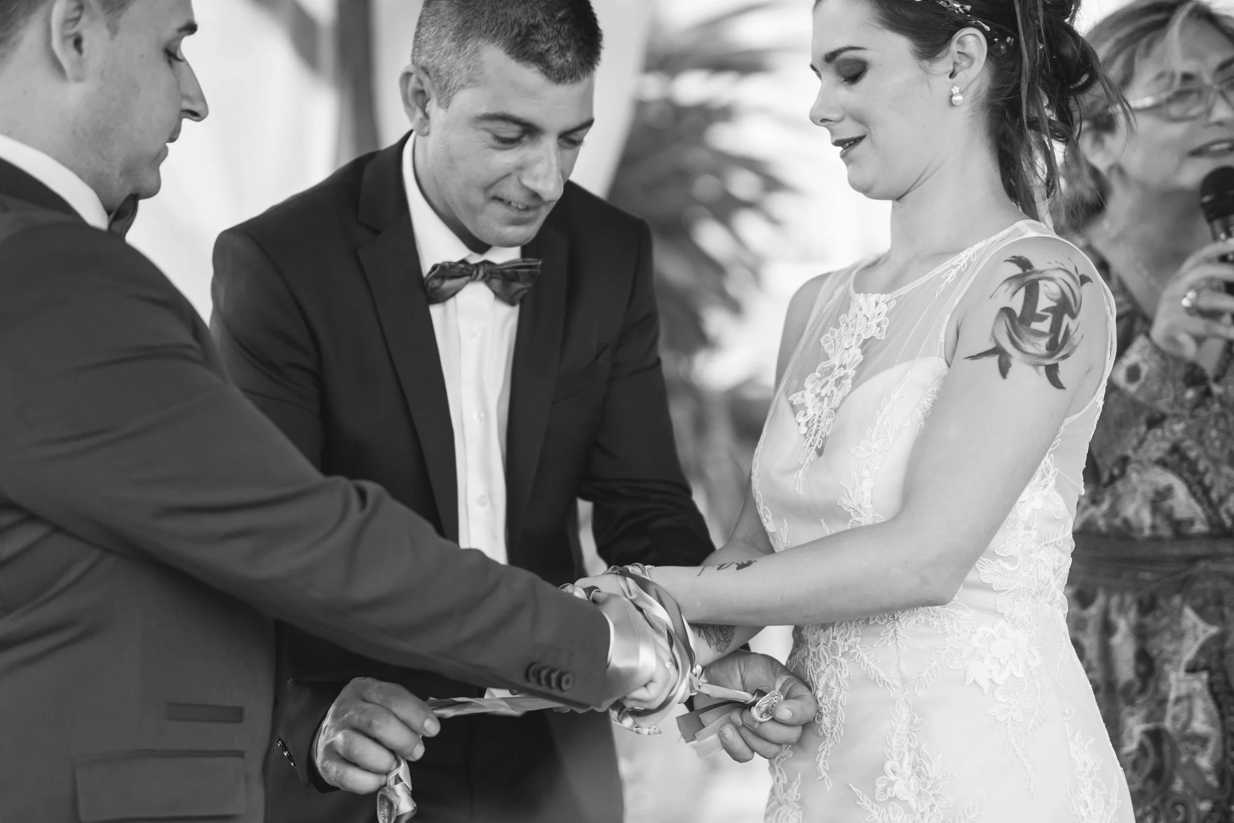 Pareja de recién casados intercambiando anillos durante la ceremonia con un oficiante y asistentes presentes.