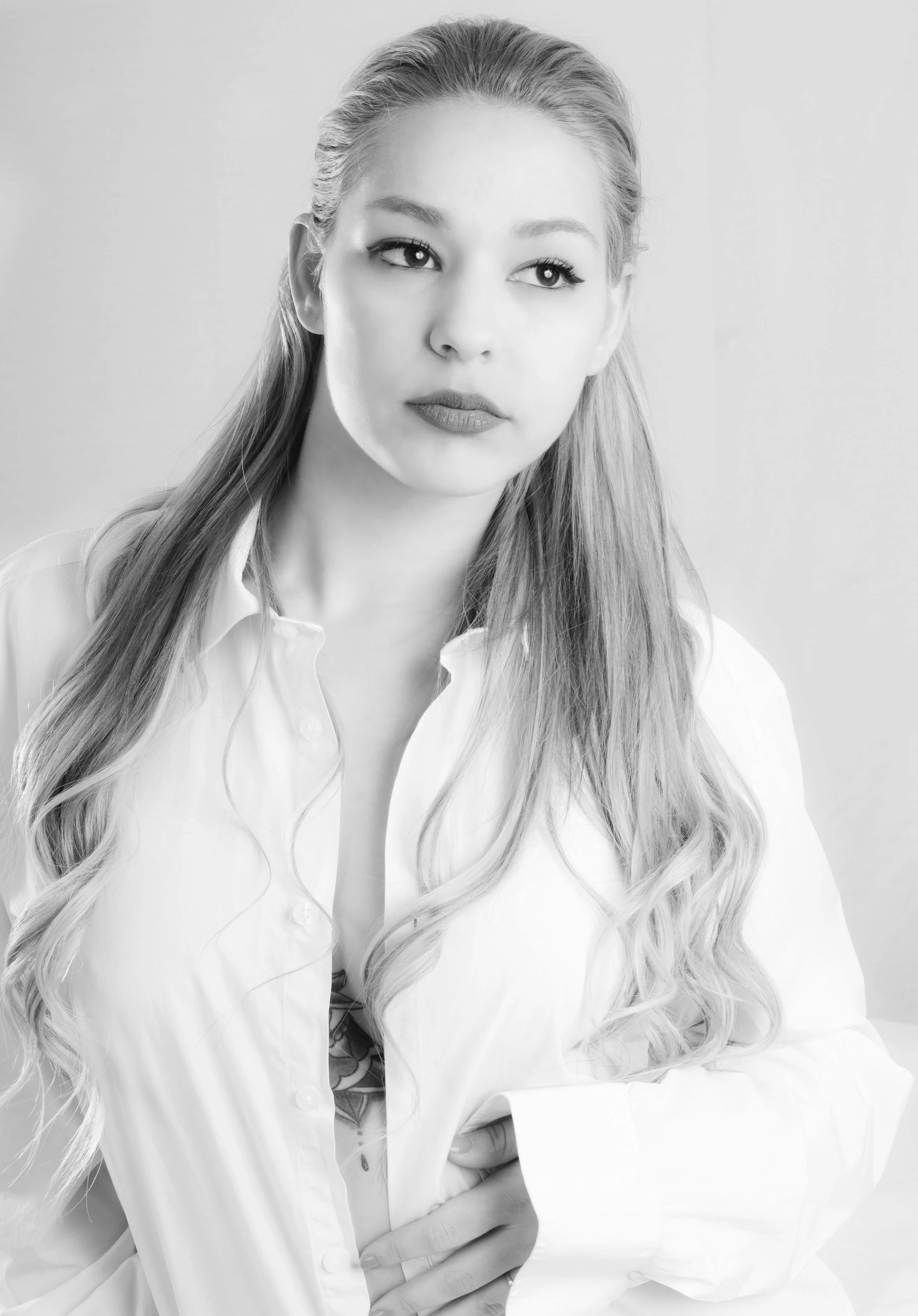 Retrato en blanco y negro de una mujer joven con cabello largo y rubio, vestida con una camisa blanca, con expresión pensativa o tranquila, frente a un fondo difuso.