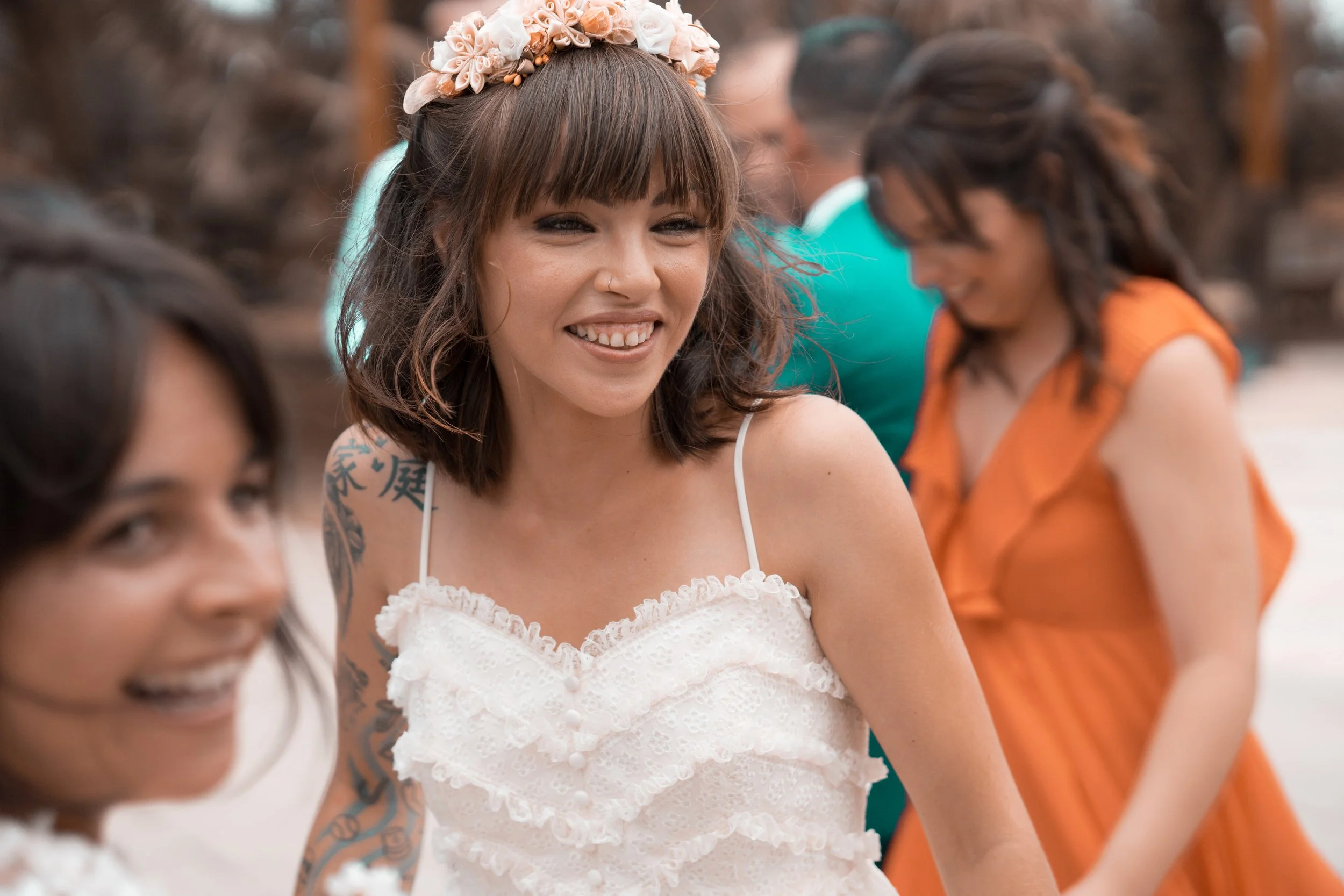 Grupo de mujeres sonriendo y disfrutando en una ocasión especial, con una mujer en el centro usando vestido blanco y una diadema de flores.