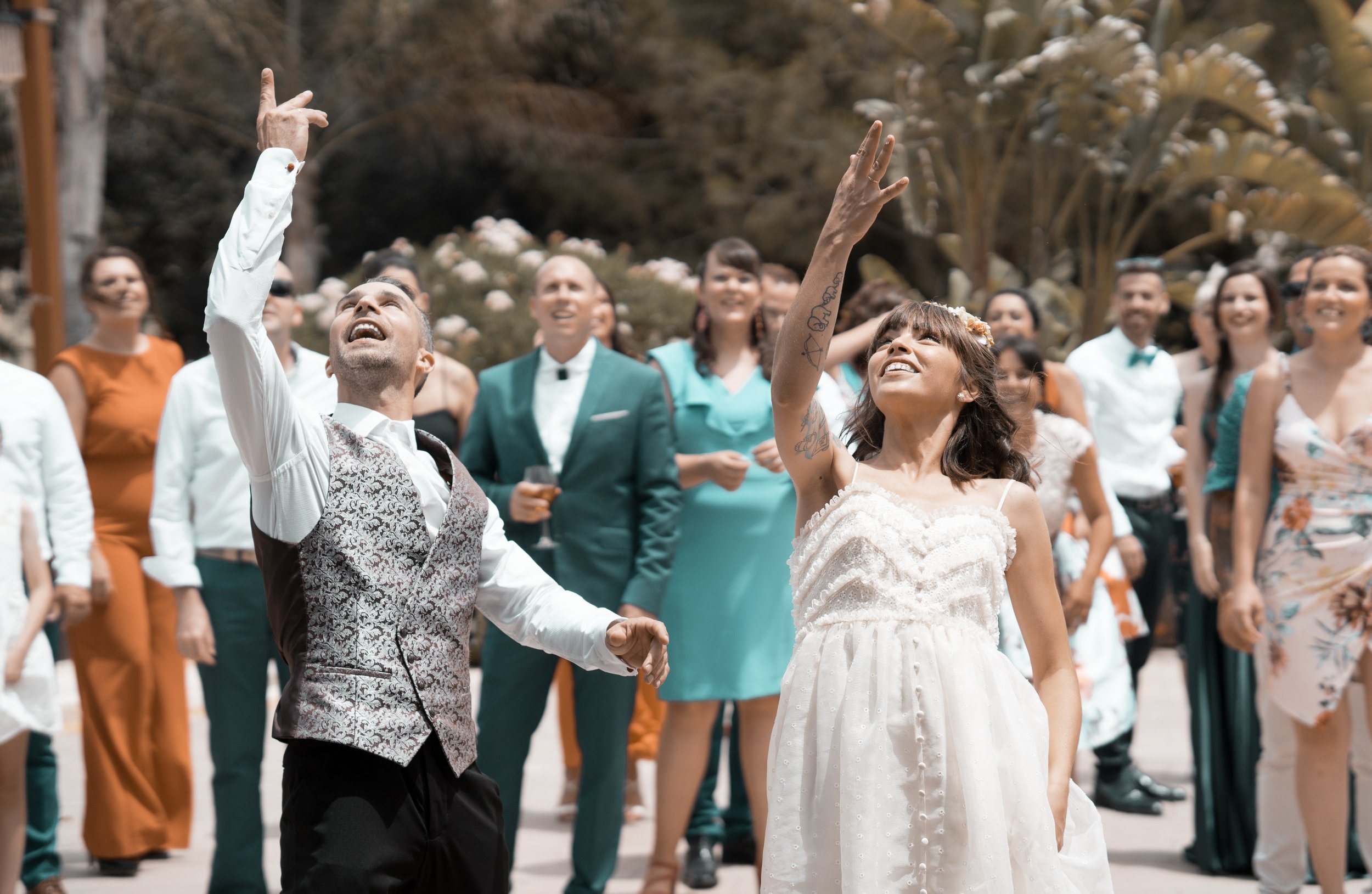 Una pareja de novios bailando en su boda, rodeados de amigos y familiares que los observan y sonríen.