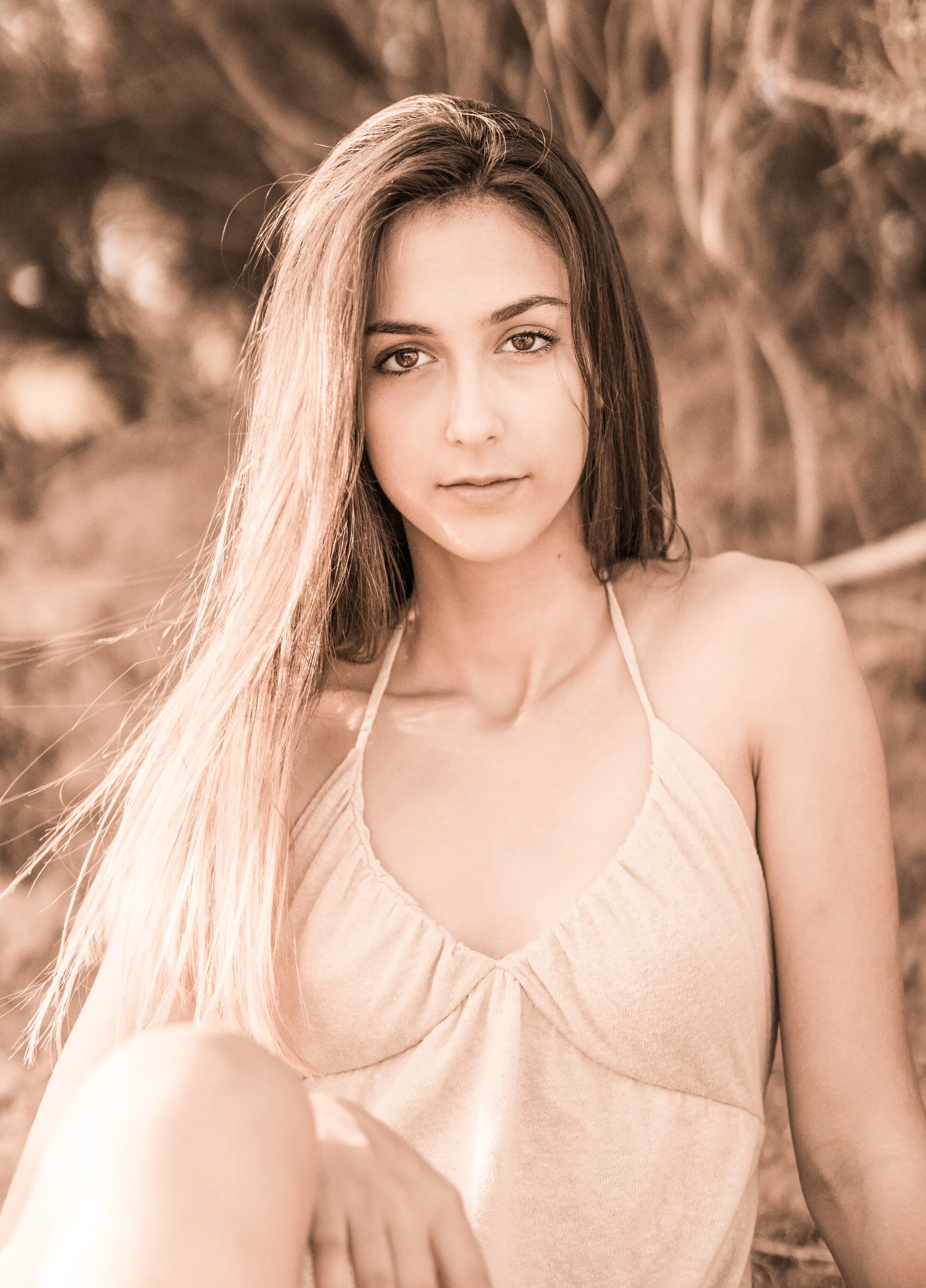 Retrato de una joven con cabello largo y rubio, usando un vestido sin mangas, en un entorno natural con fondo borroso.