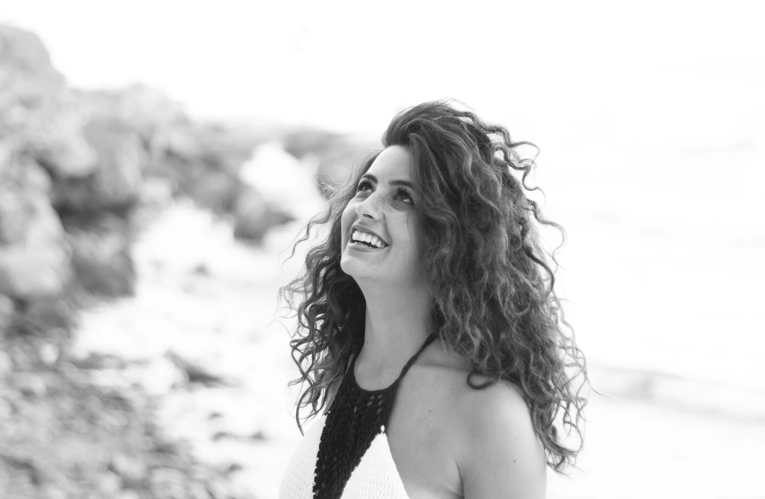 Mujer sonriendo en la playa con cabello rizado, vista en blanco y negro.