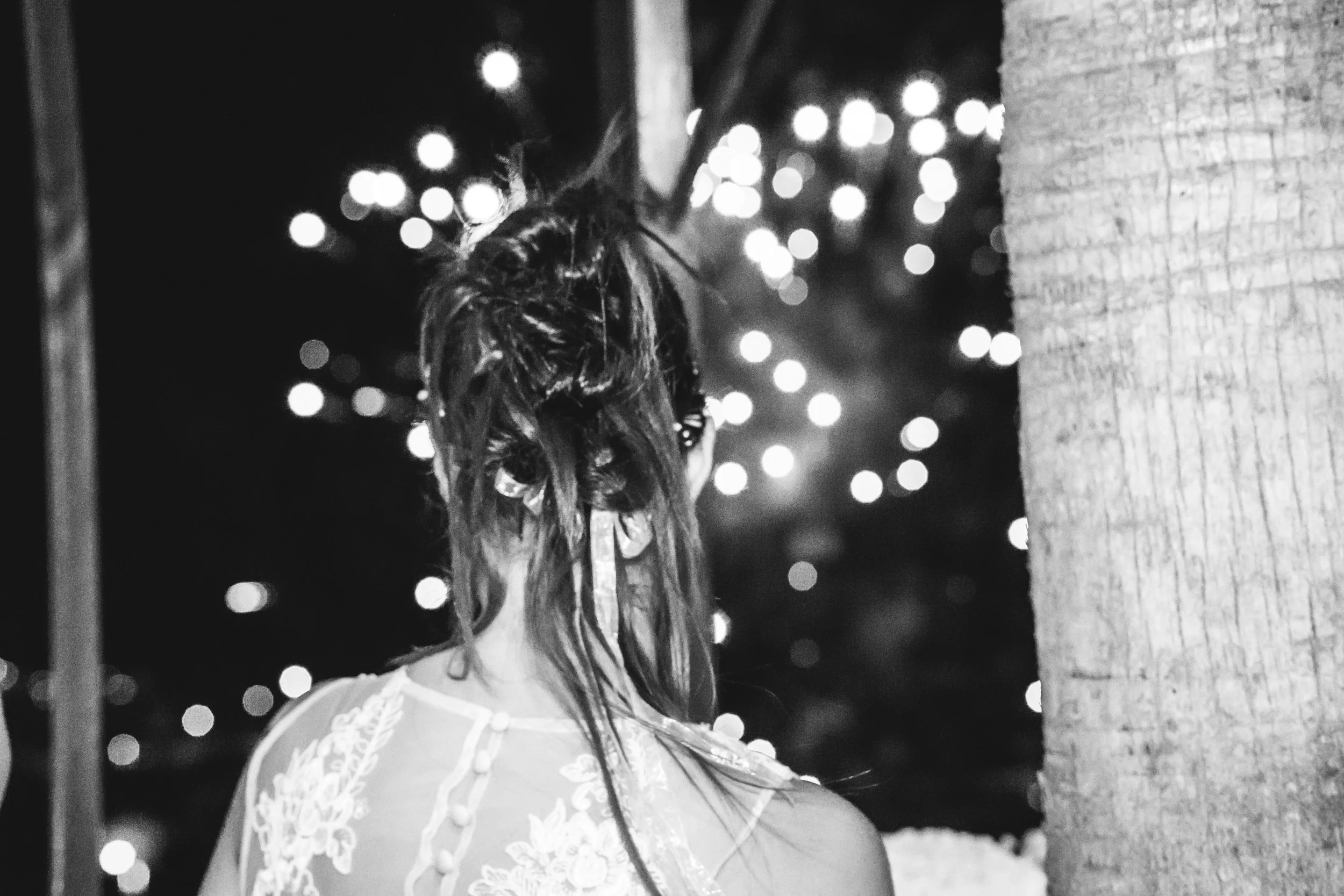 Mujer con cabello en dreadlocks, vista desde atrás, con fondo de luces borrosas en la noche.