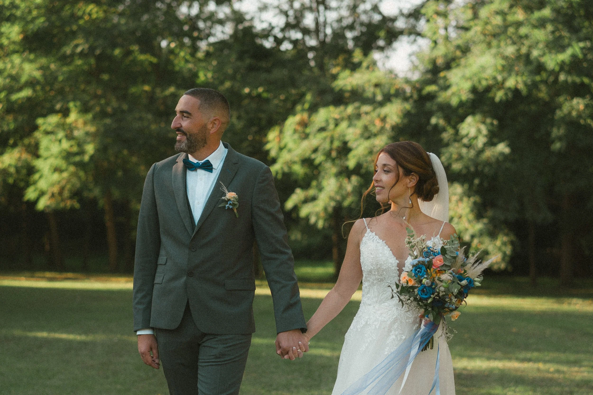 Un couple de mariés marchant main dans la main dans un parc verdoyant lors d'un mariage en plein air.