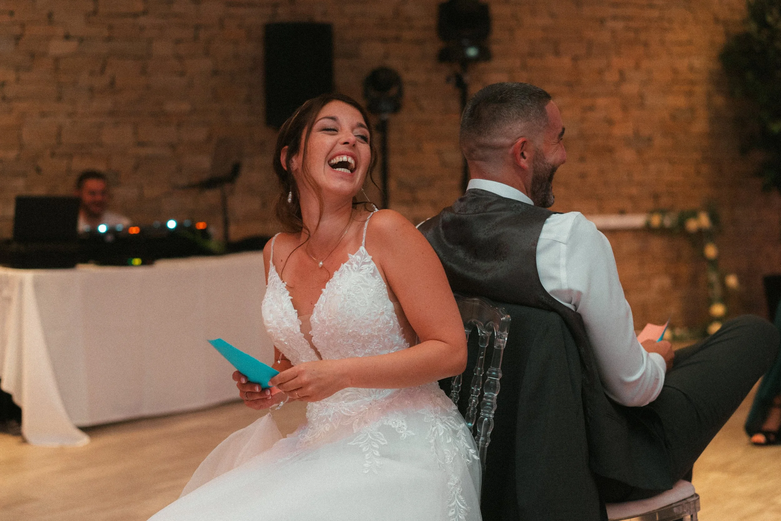 Une mariée en robe blanche rit, assise à côté d'un homme en veston, lors d'une cérémonie de mariage.
