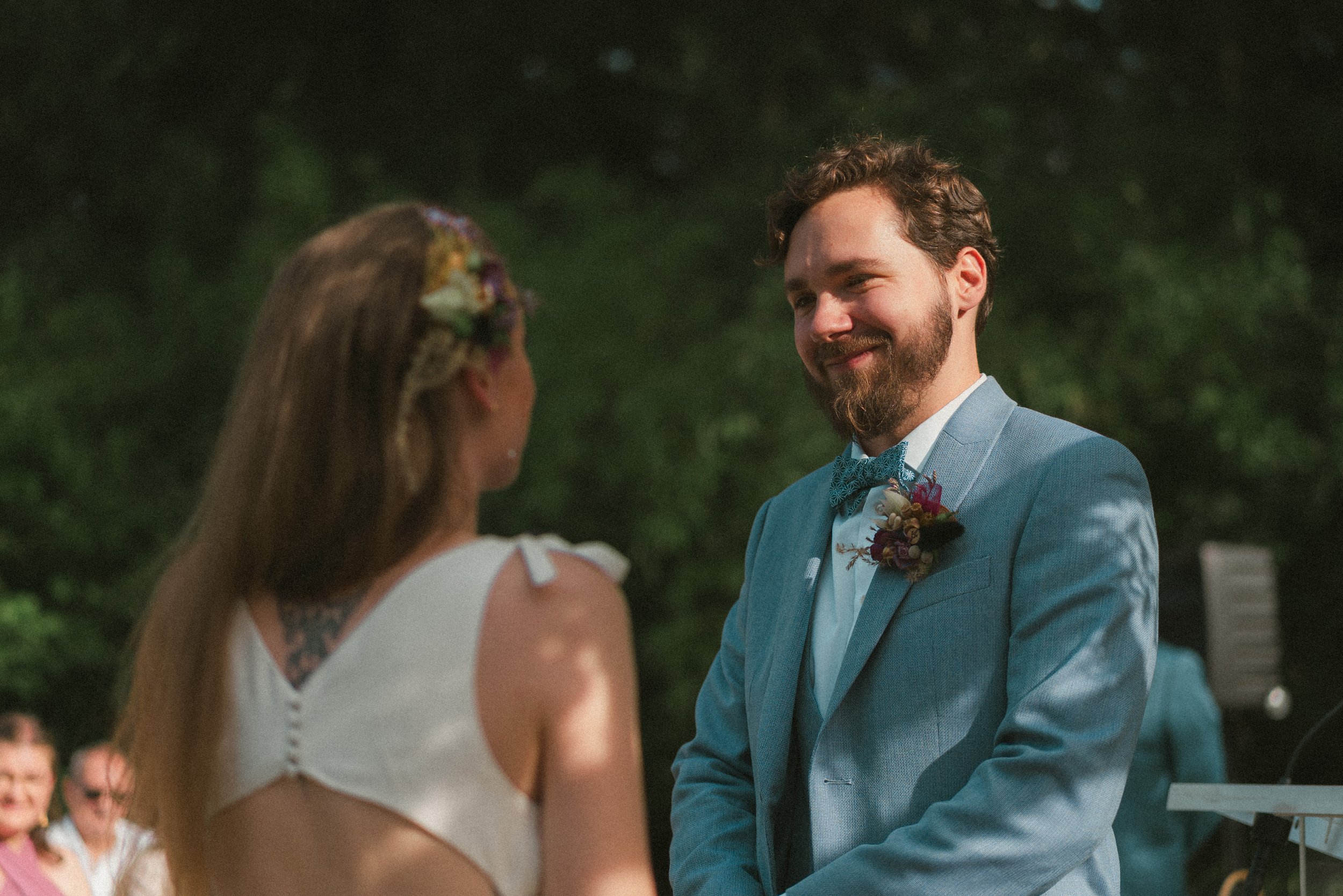 Un homme et une femme échangent un regard lors d'un mariage en plein air, avec des invités en arrière-plan