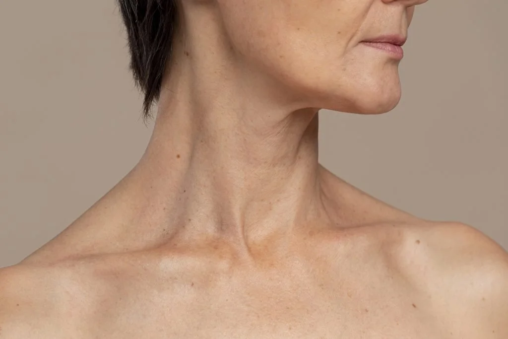 Close-up of a middle-aged woman's bare shoulder, neck, and lower face, showing natural skin texture and slight signs of aging.