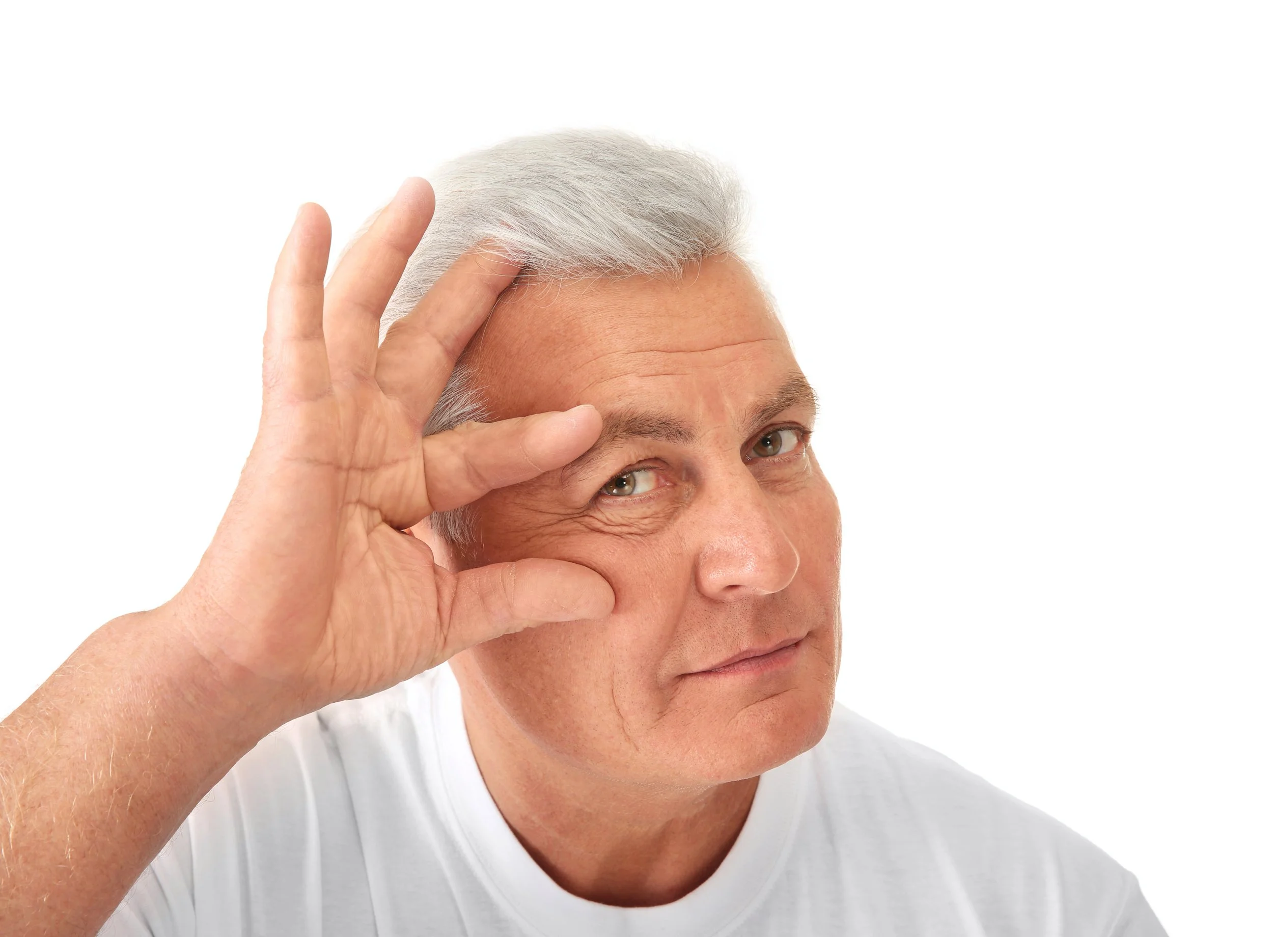 Older man with gray hair making a circle with his hand around his eye, smiling at the camera, wearing a white shirt against a plain white background.