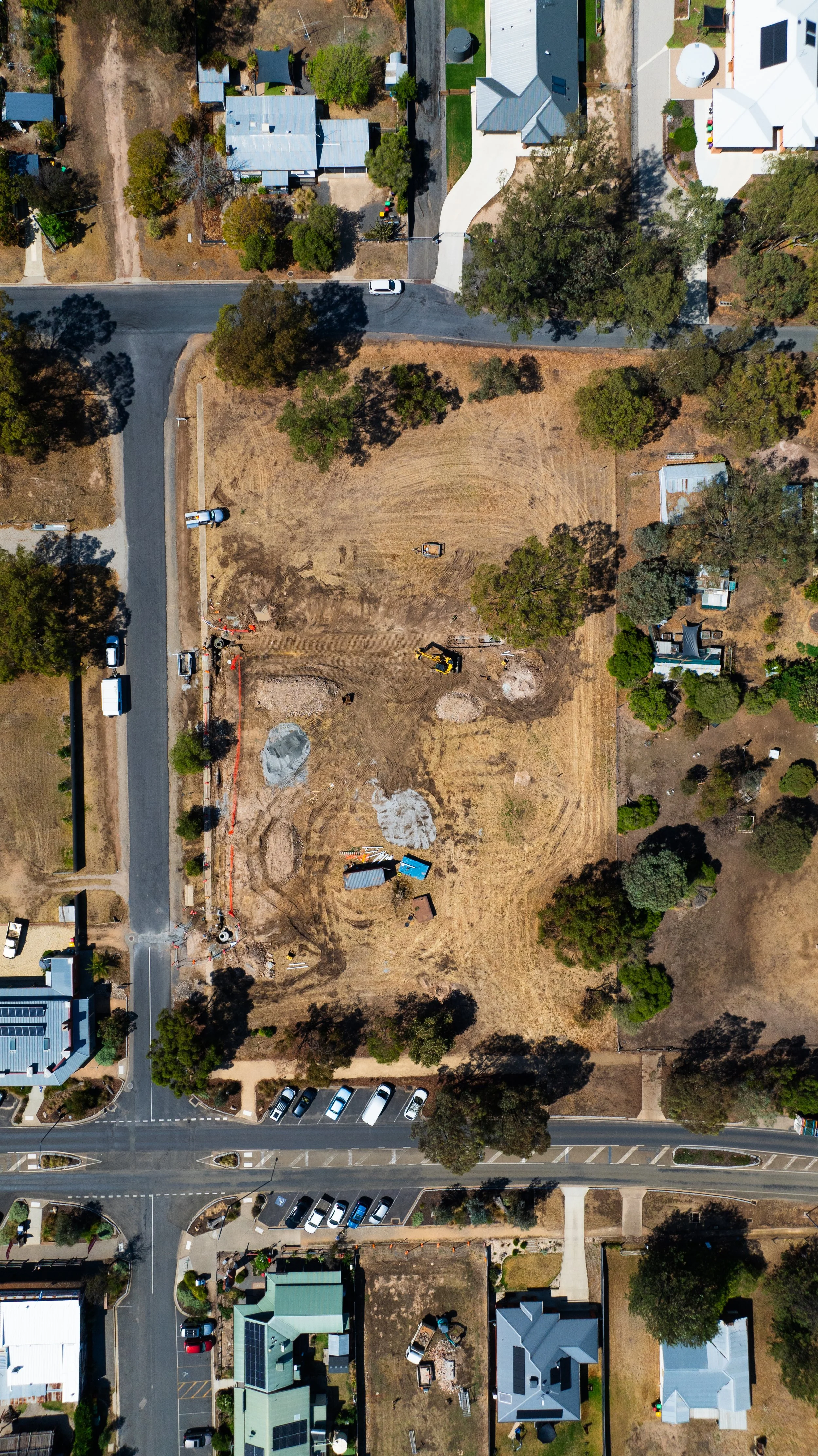 An aerial view of a neighborhood with houses, trees, roads, and a large construction site in the middle.