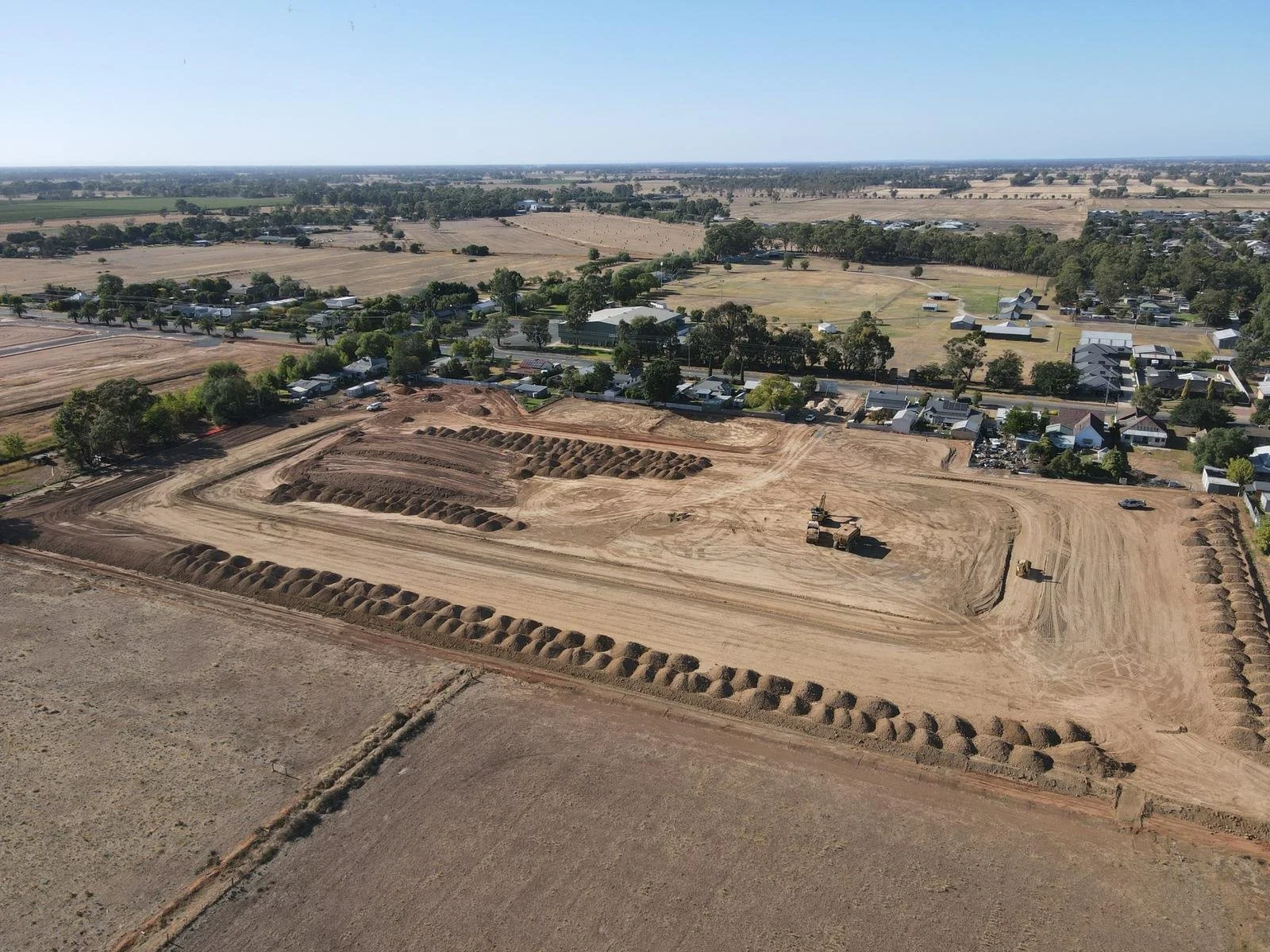 Aerial view of a construction site with machinery, dirt piles, and a partially developed area, surrounded by farmland and residential homes.