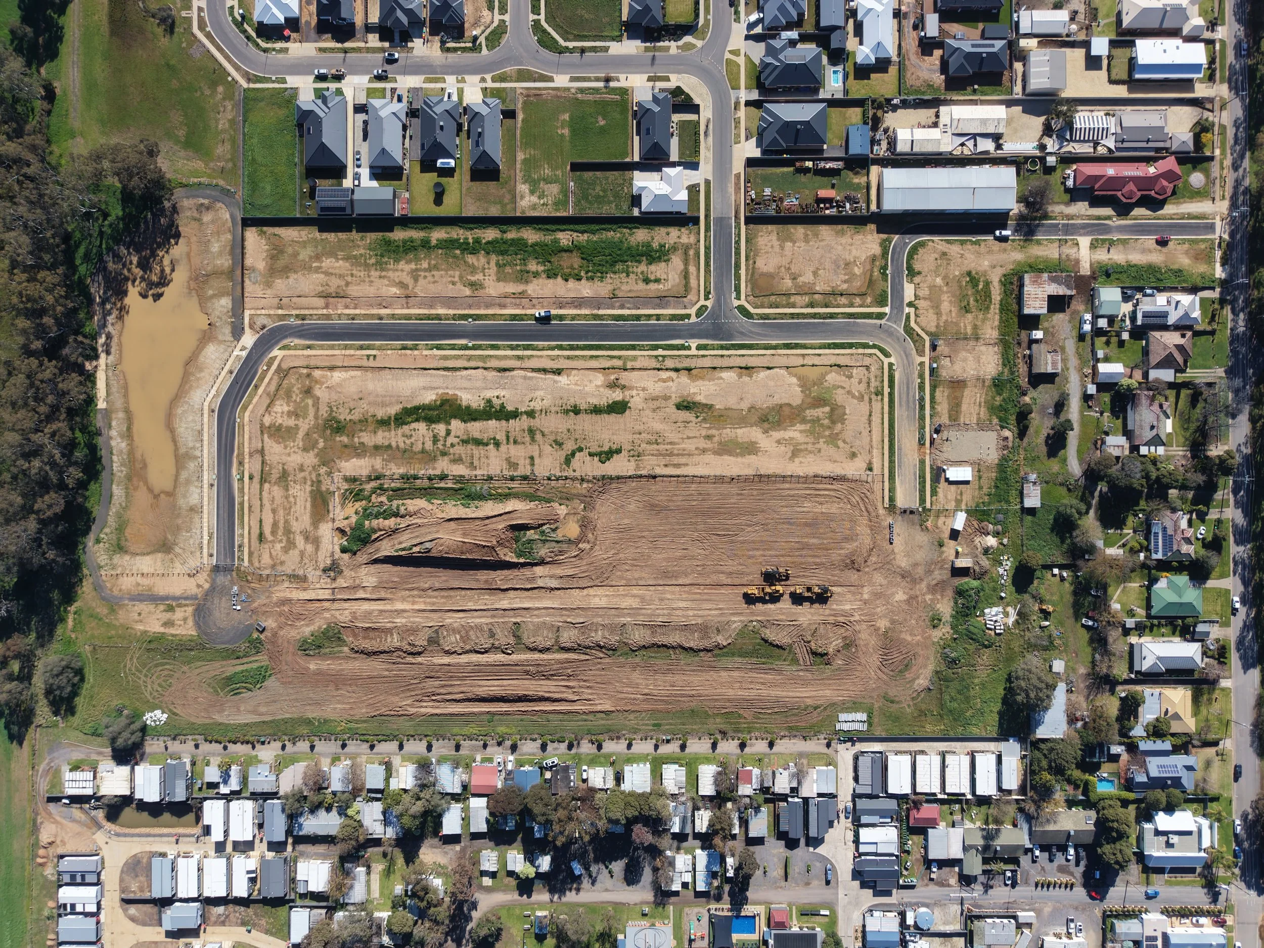 An aerial view of a residential area with houses, streets, and a construction site with cleared land and construction equipment.