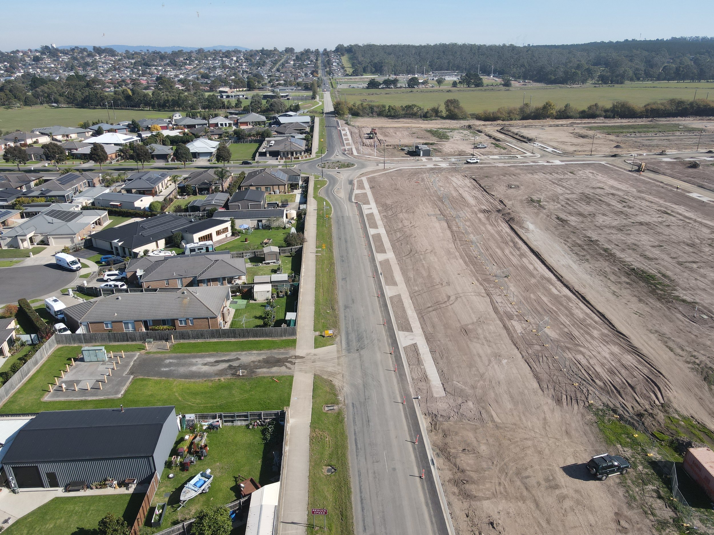 An aerial view of a residential neighborhood with houses and trees on the left side, and a construction site with cleared land and construction vehicles on the right side.