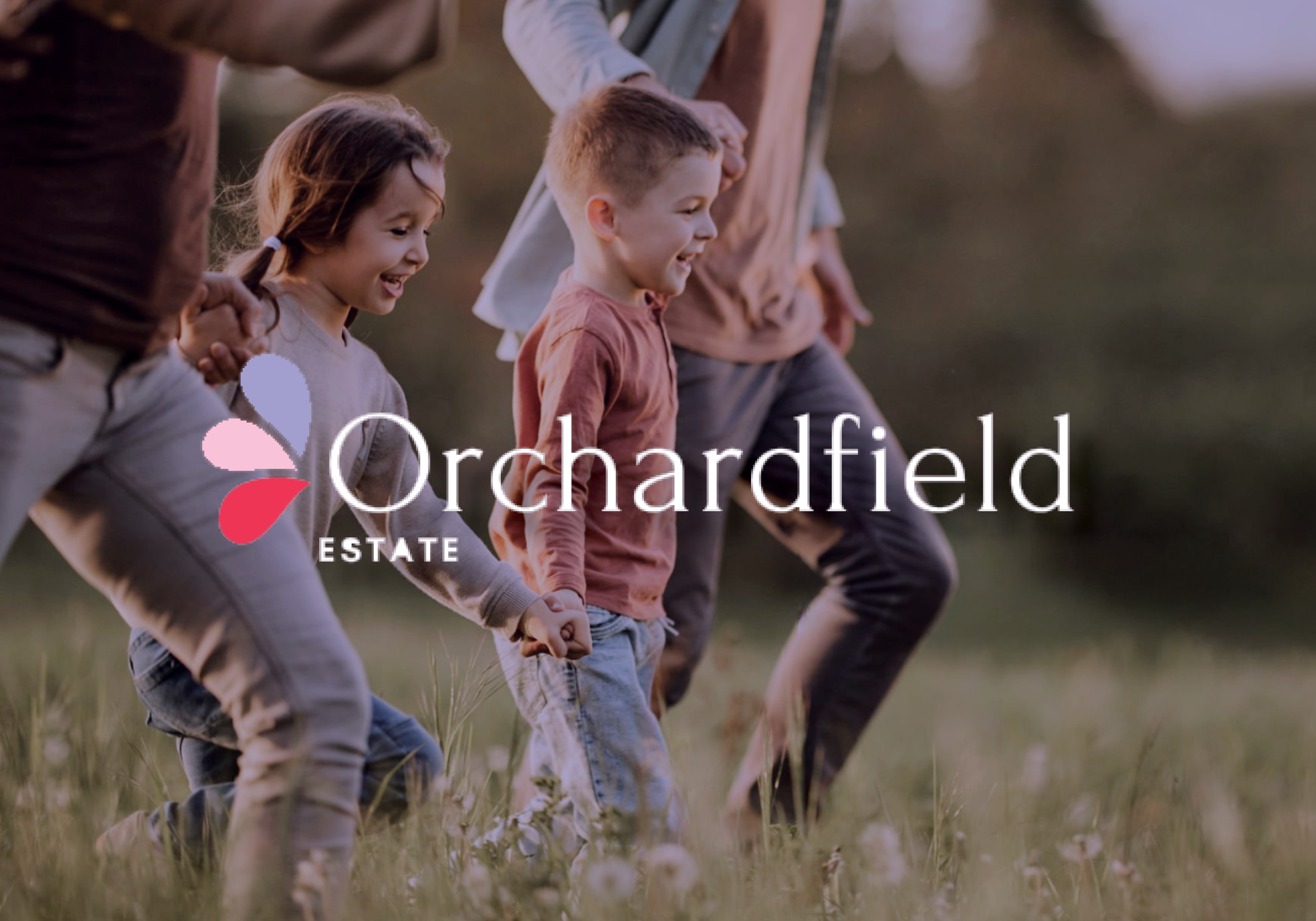 Children holding hands and walking together in a field during sunset, with Orchardfield Estate logo overlayed in the bottom left corner.