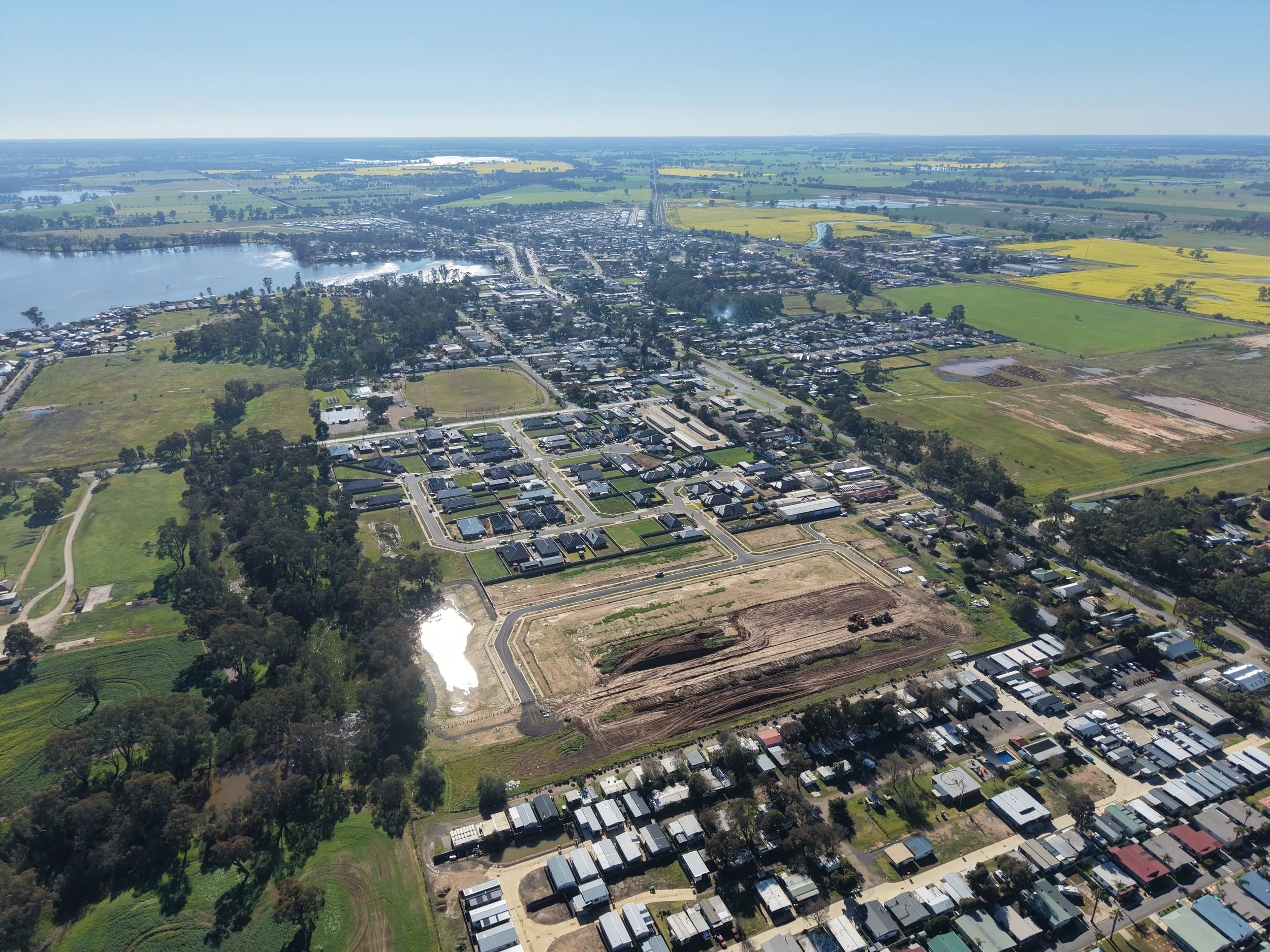 Aerial view of a small town with a lake, fields, and residential area on a clear day.