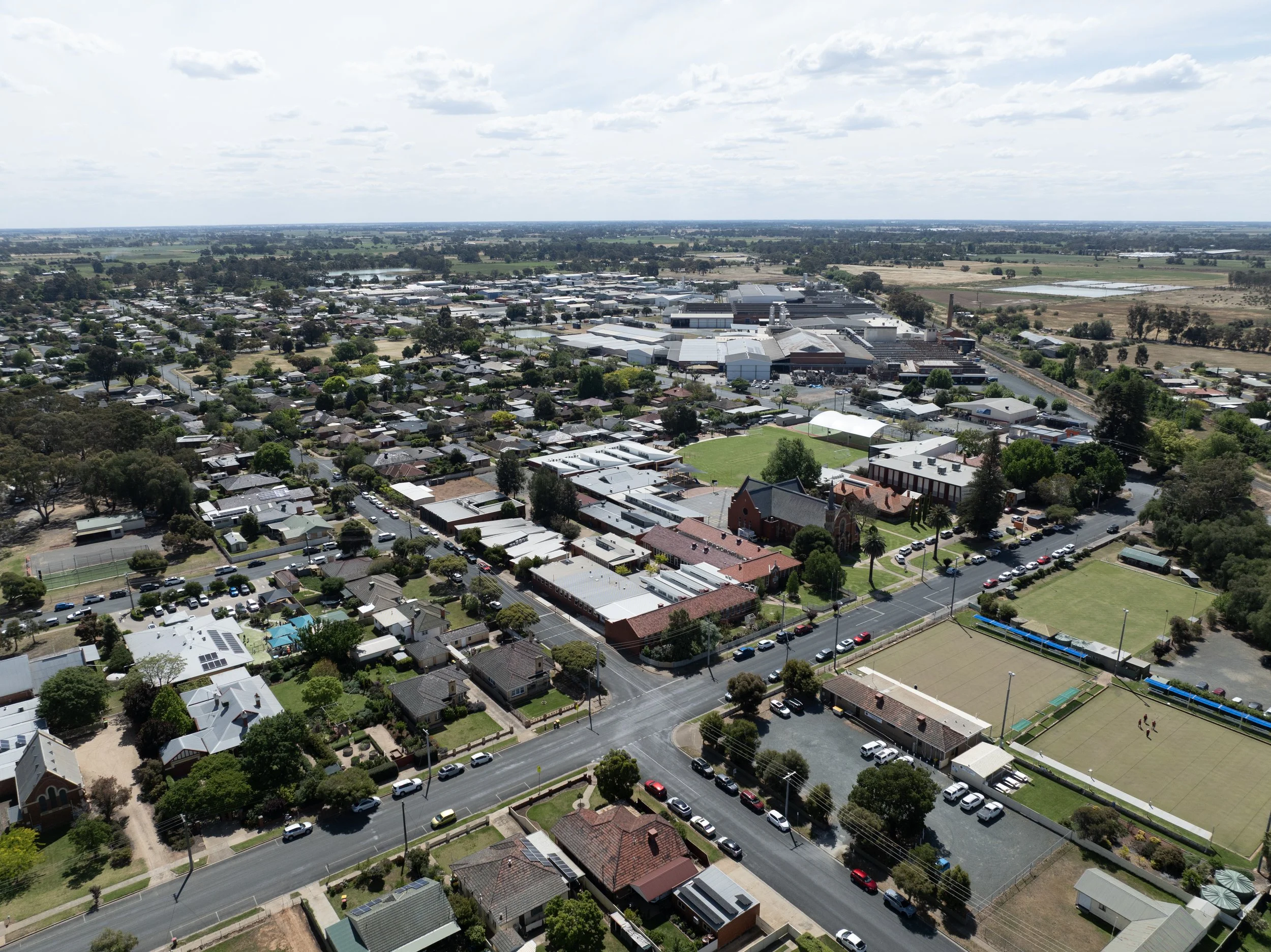 Aerial view of a suburban area with houses, streets, and a large industrial or commercial complex surrounded by open land and fields.
