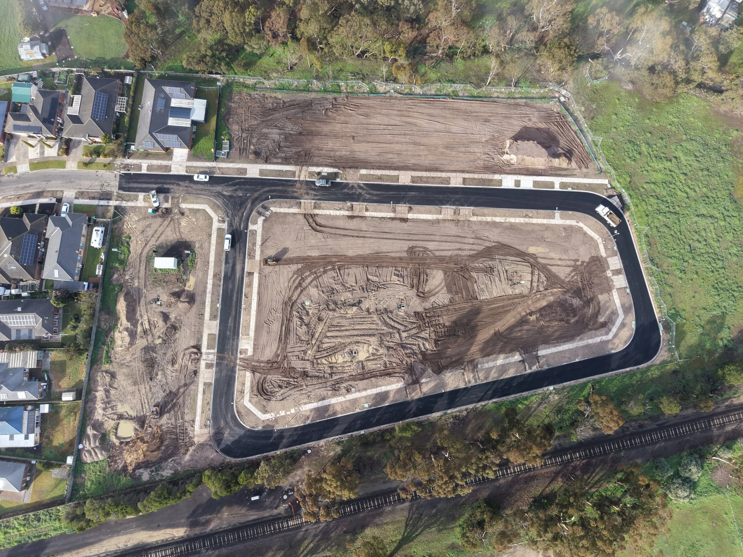 An aerial view of a residential neighborhood with homes, roads, and a large construction site with dirt and equipment.