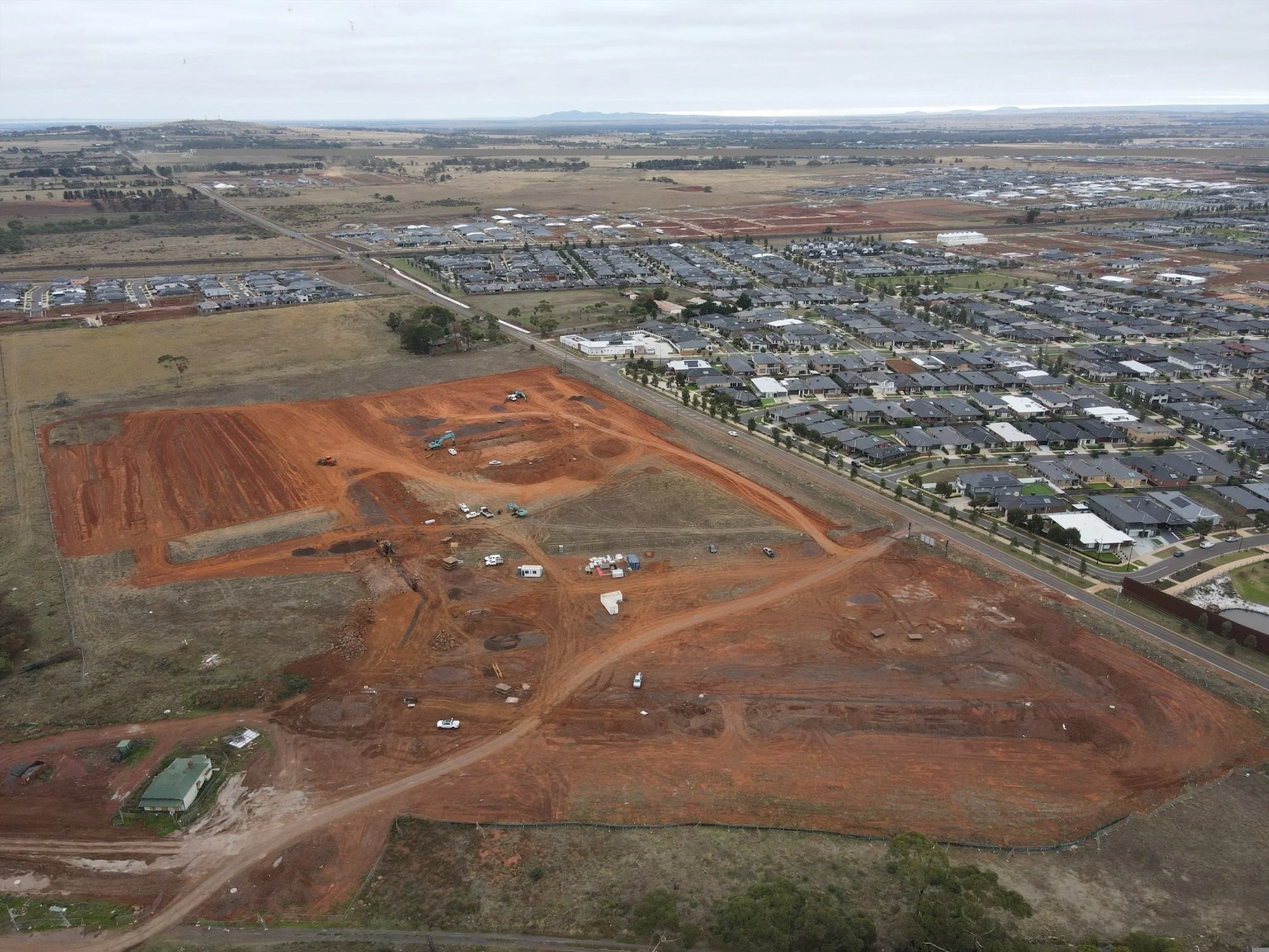 An aerial view of a suburban area with houses, roads, and farmland under construction.