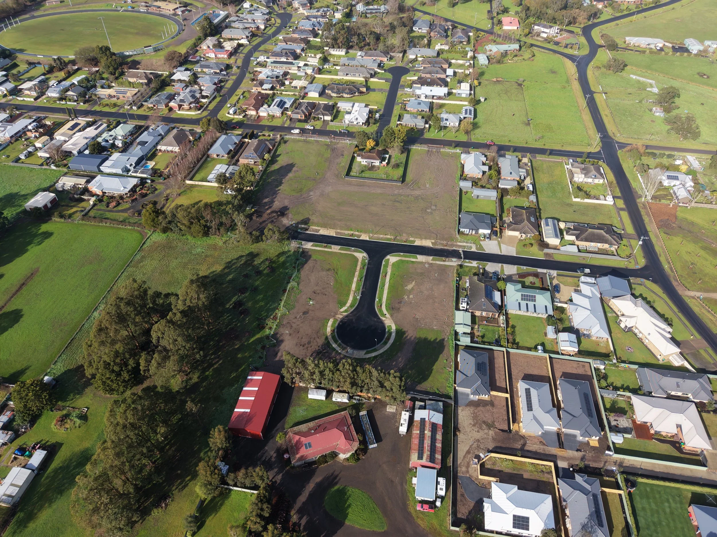 An aerial view of a suburban neighborhood with houses, streets, trees, and a large green field with a sports track.