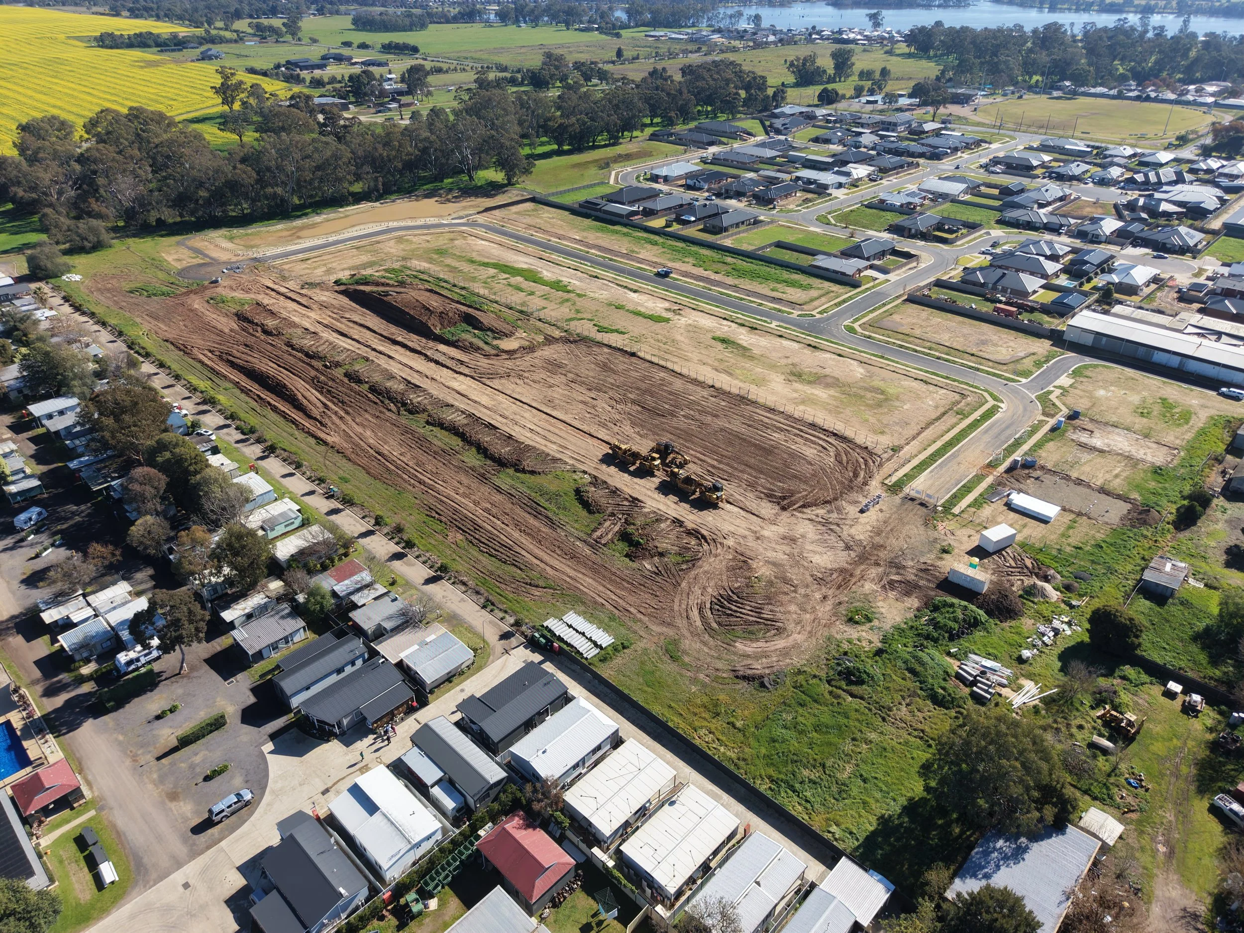 Aerial view of a residential area with houses, roads under construction, and green fields.