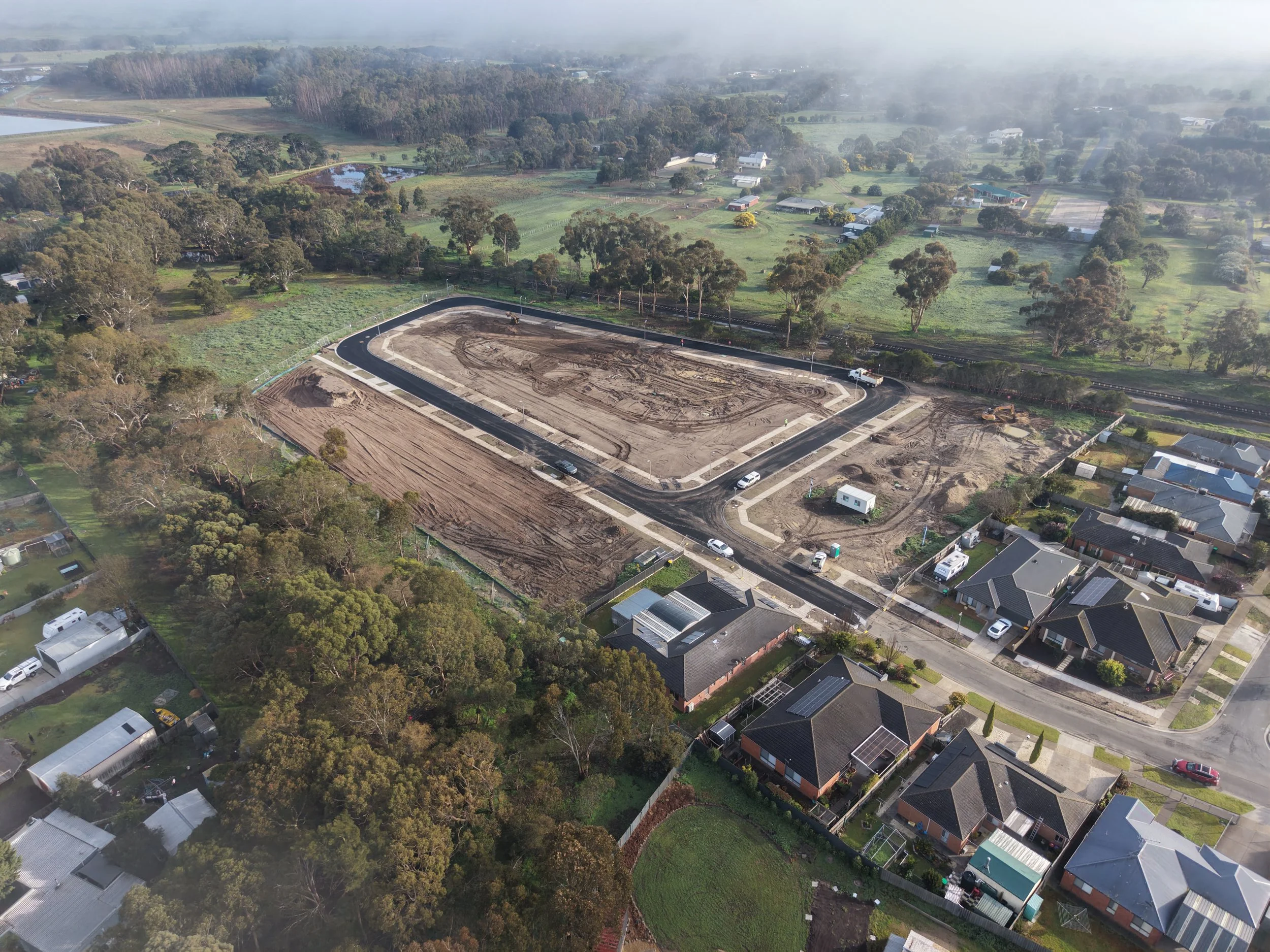 Aerial view of a residential neighborhood with houses, trees, and a construction site with cleared land and dirt tracks.
