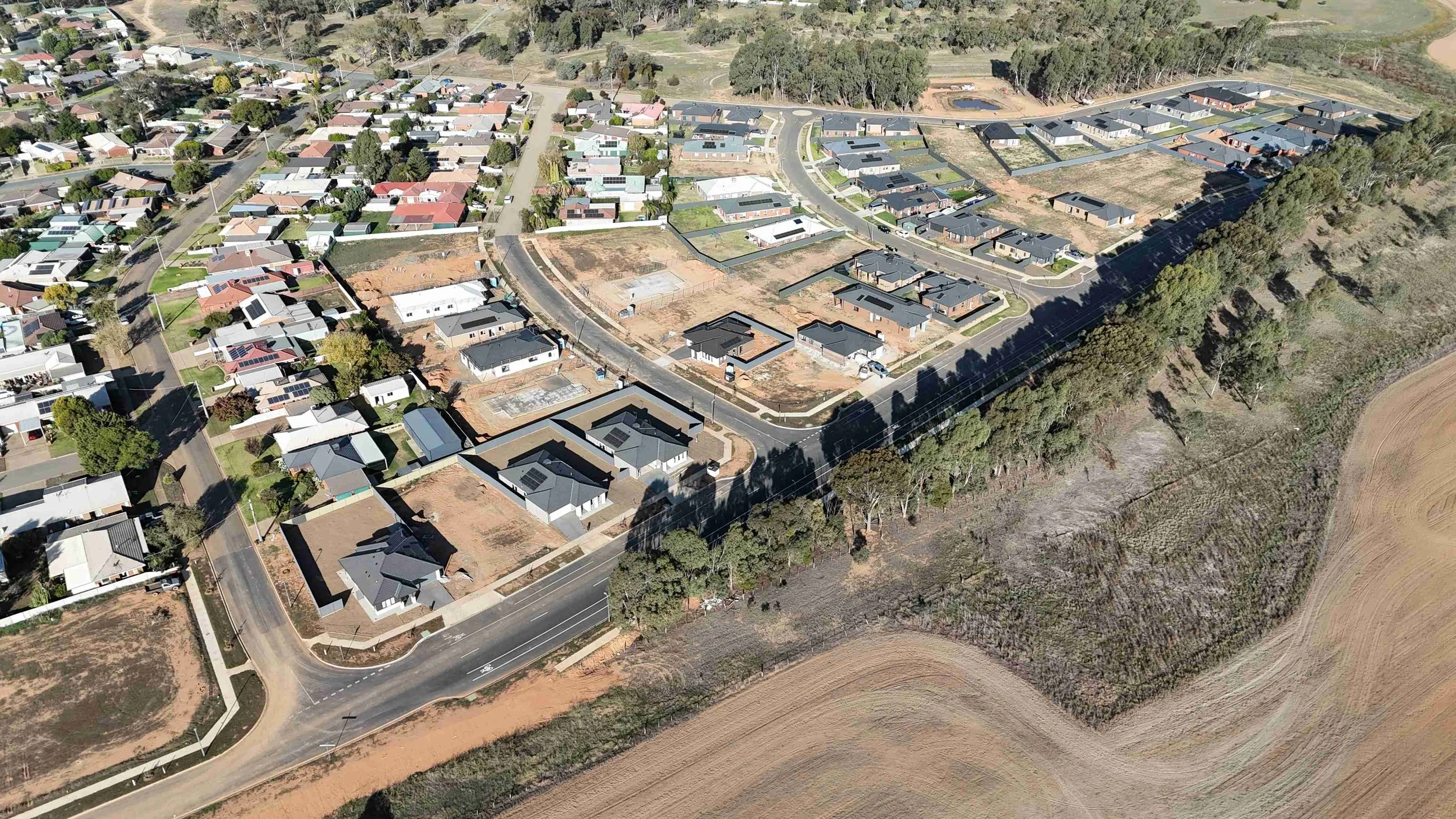 An aerial view of a residential neighborhood with a mix of completed houses and empty plots under construction, surrounded by trees and open land.