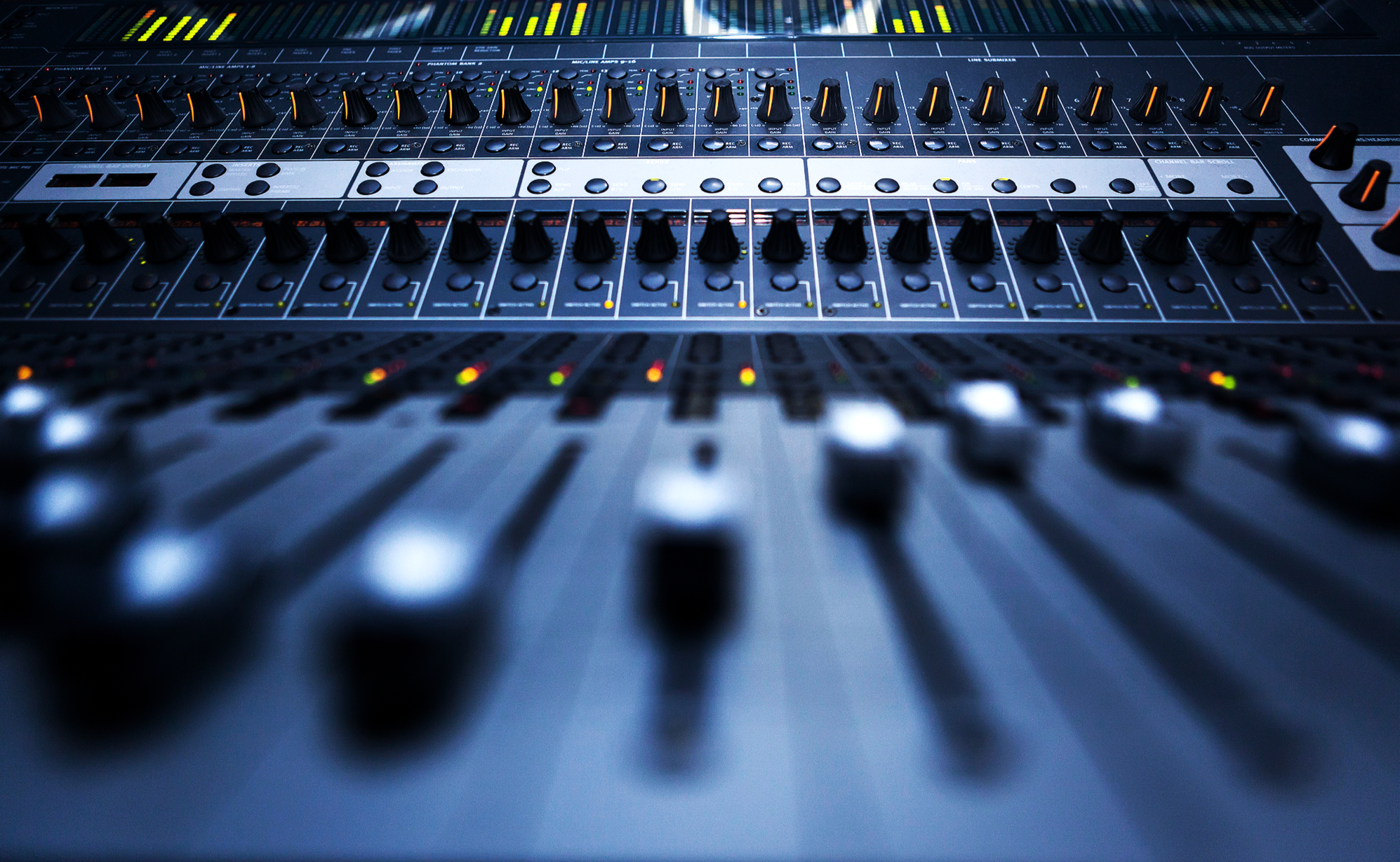 Close-up of an audio mixing console with various knobs, buttons, and sliders in a professional recording studio.