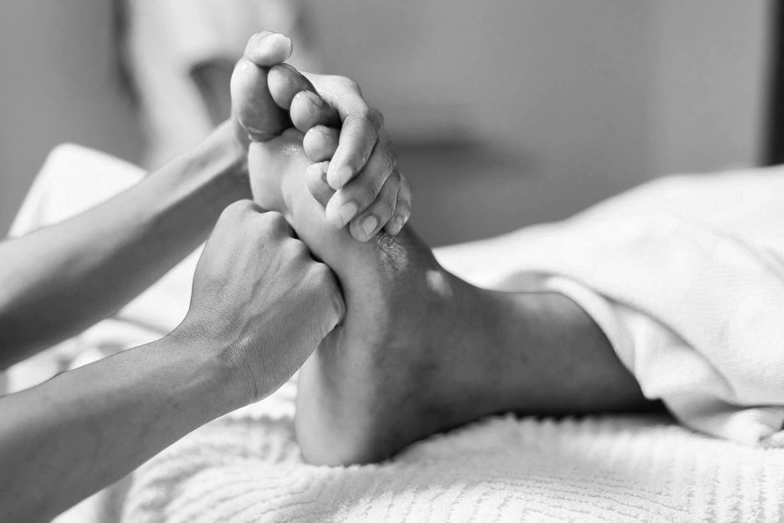 Person giving a foot massage or physiotherapy to another person's foot in black and white.
