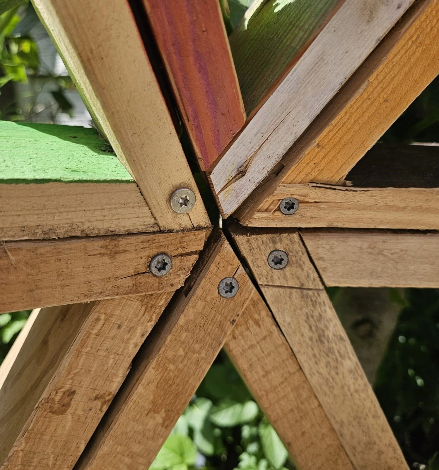 Close-up view of a wooden structure assembled with screws, showing the joints and different colors of the wood planks.