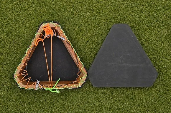 Two black triangular surfing or skateboarding beginners' ramps placed on green grass, one with orange and green ropes tied around it.